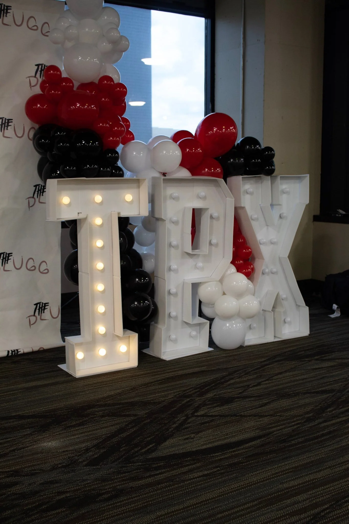 Large decorative sign spelling 'IOU' with balloons in red, black, and white colors attached to it, set up indoors near a window.