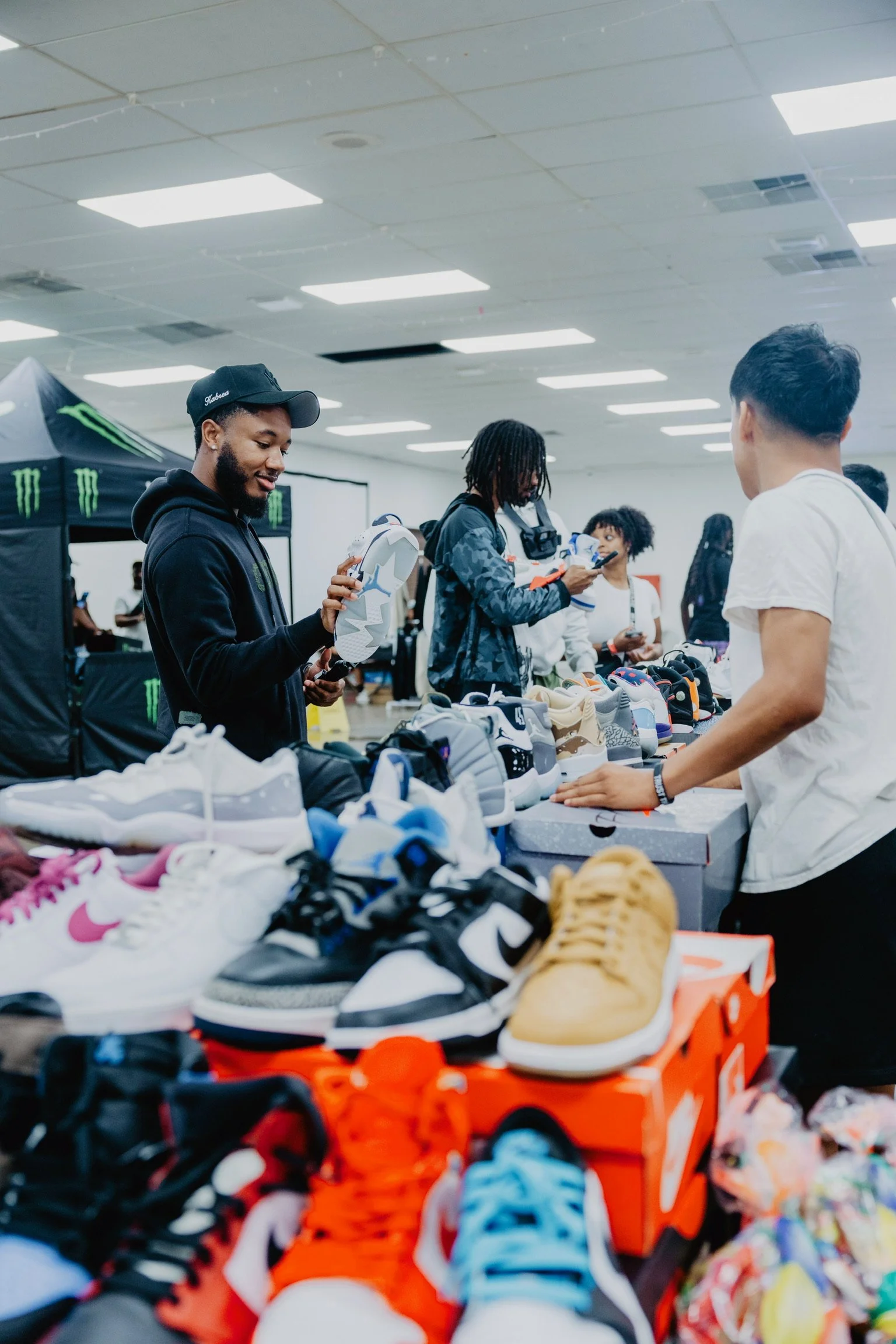People browsing and shopping sneakers at an indoor sneaker event or sale with tables displaying various sneaker styles.