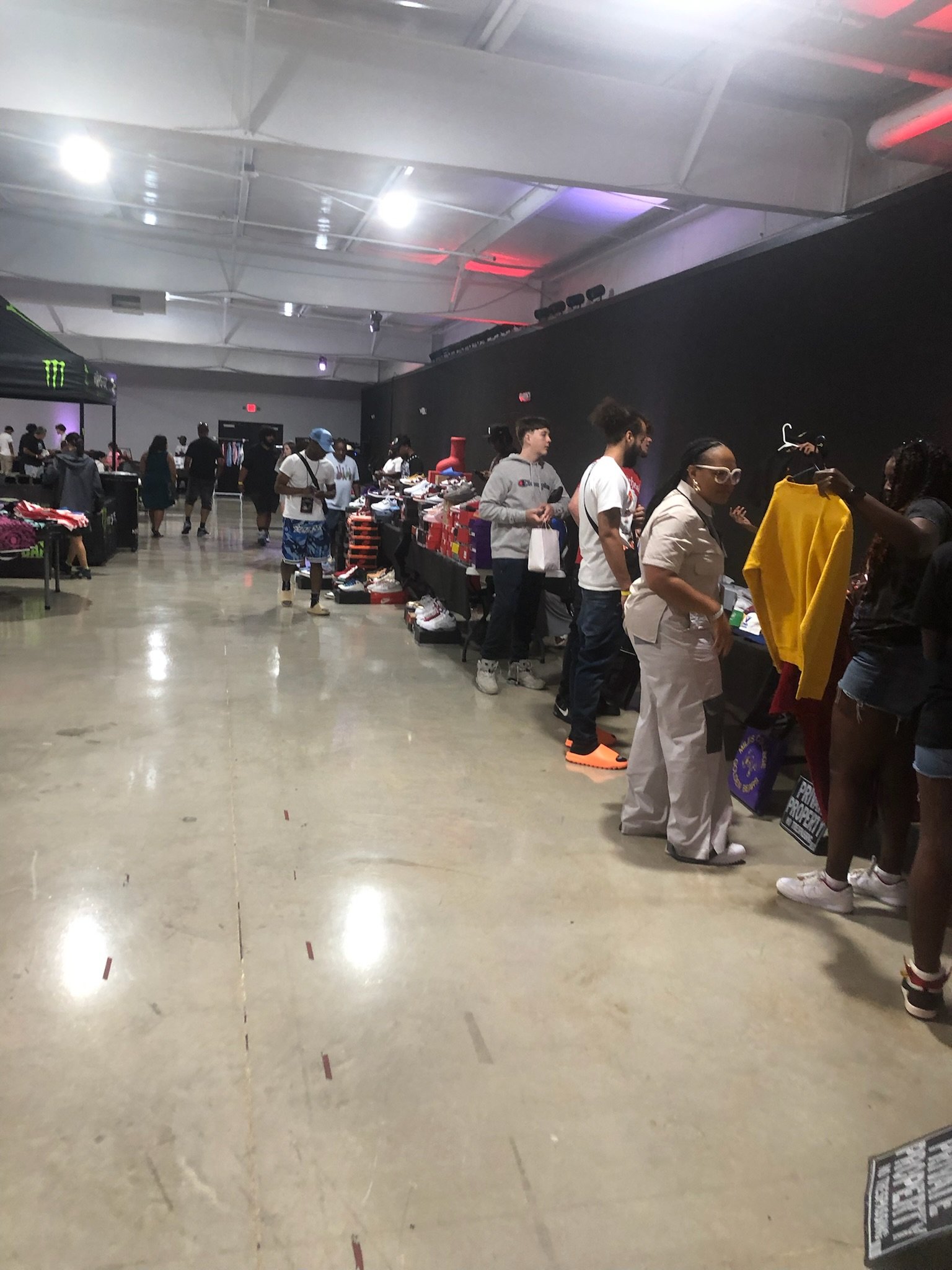 People shopping at a sneaker swap meet with tables of shoes for sale, inside a large indoor venue.