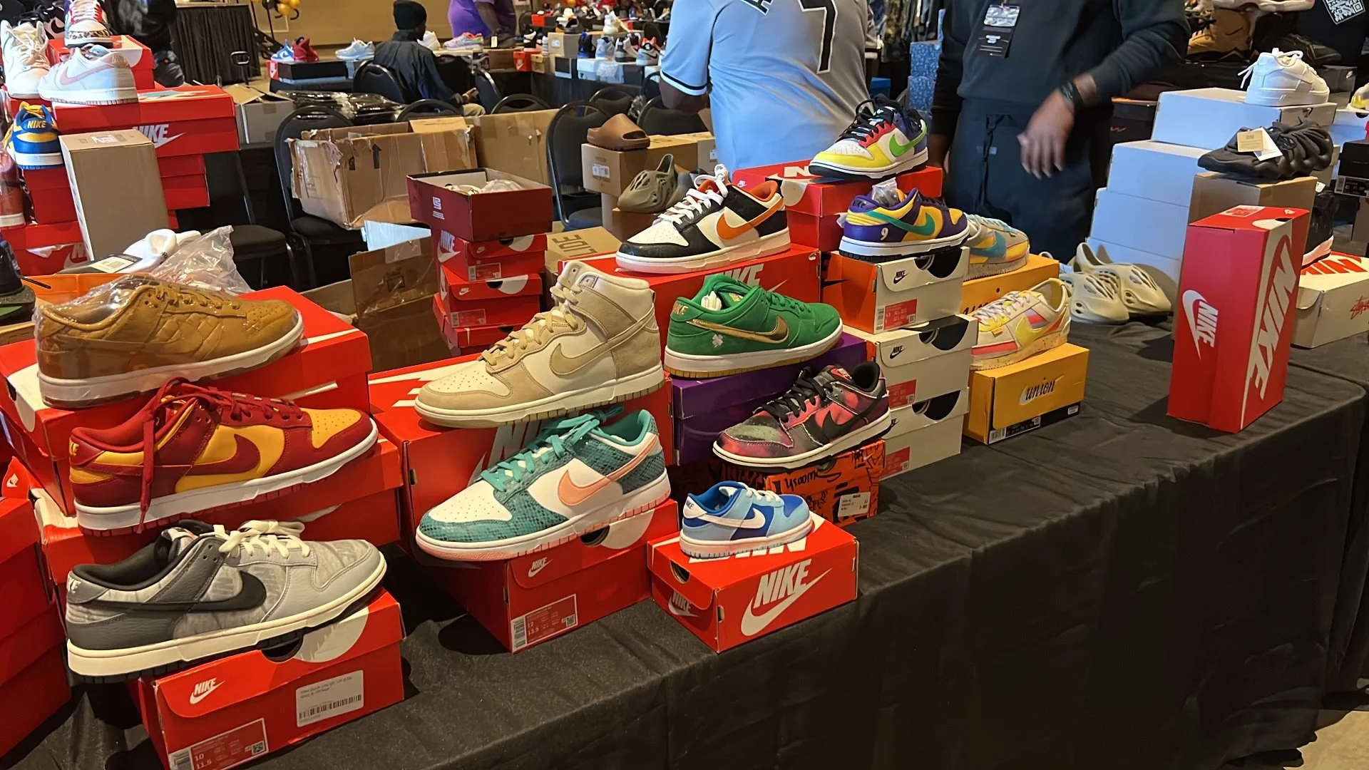 Table displaying various Nike sneakers and shoe boxes in a shoe sale event, with people browsing in the background.