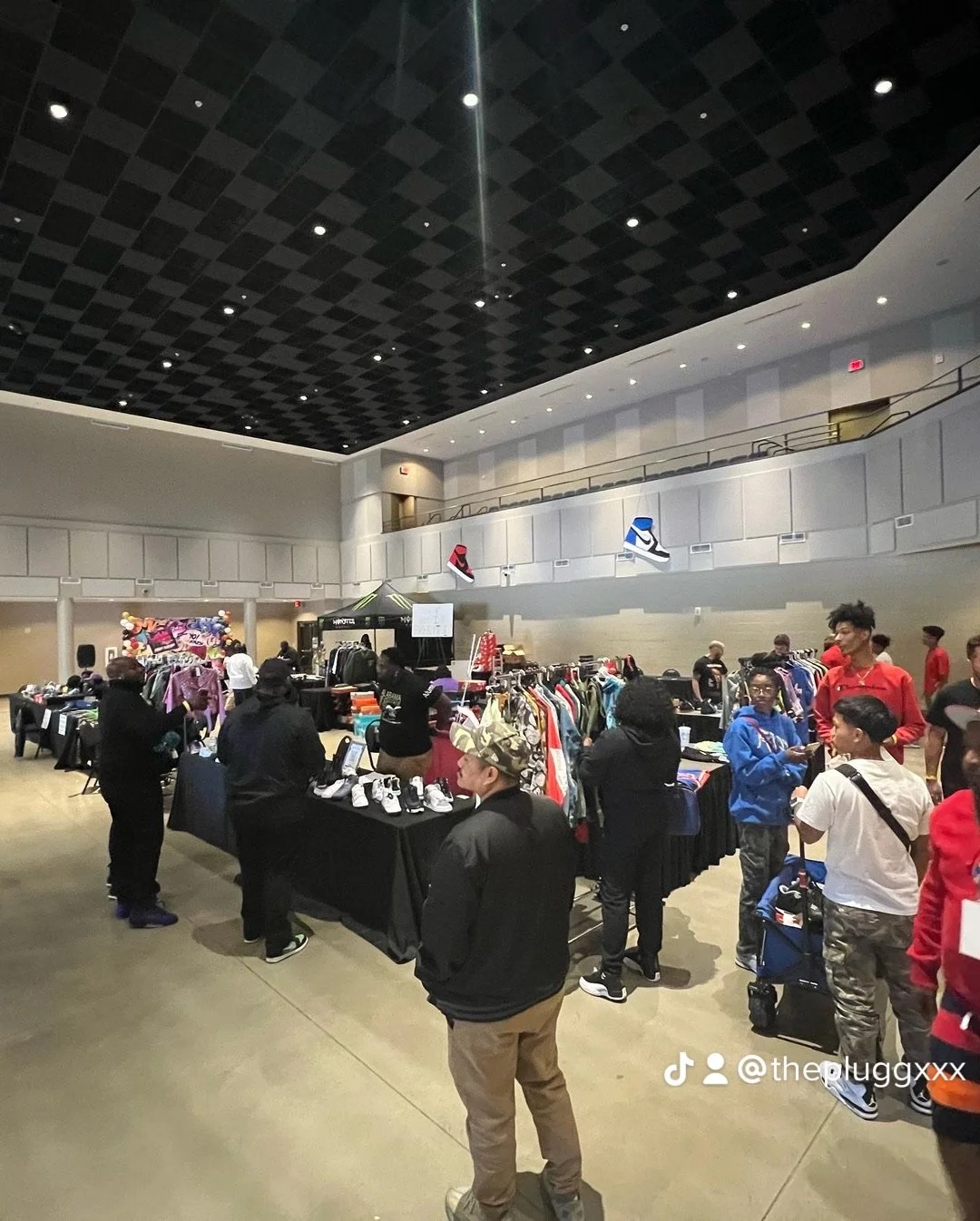 Indoor flea market with tables of clothing, shoes, and accessories, and people shopping.