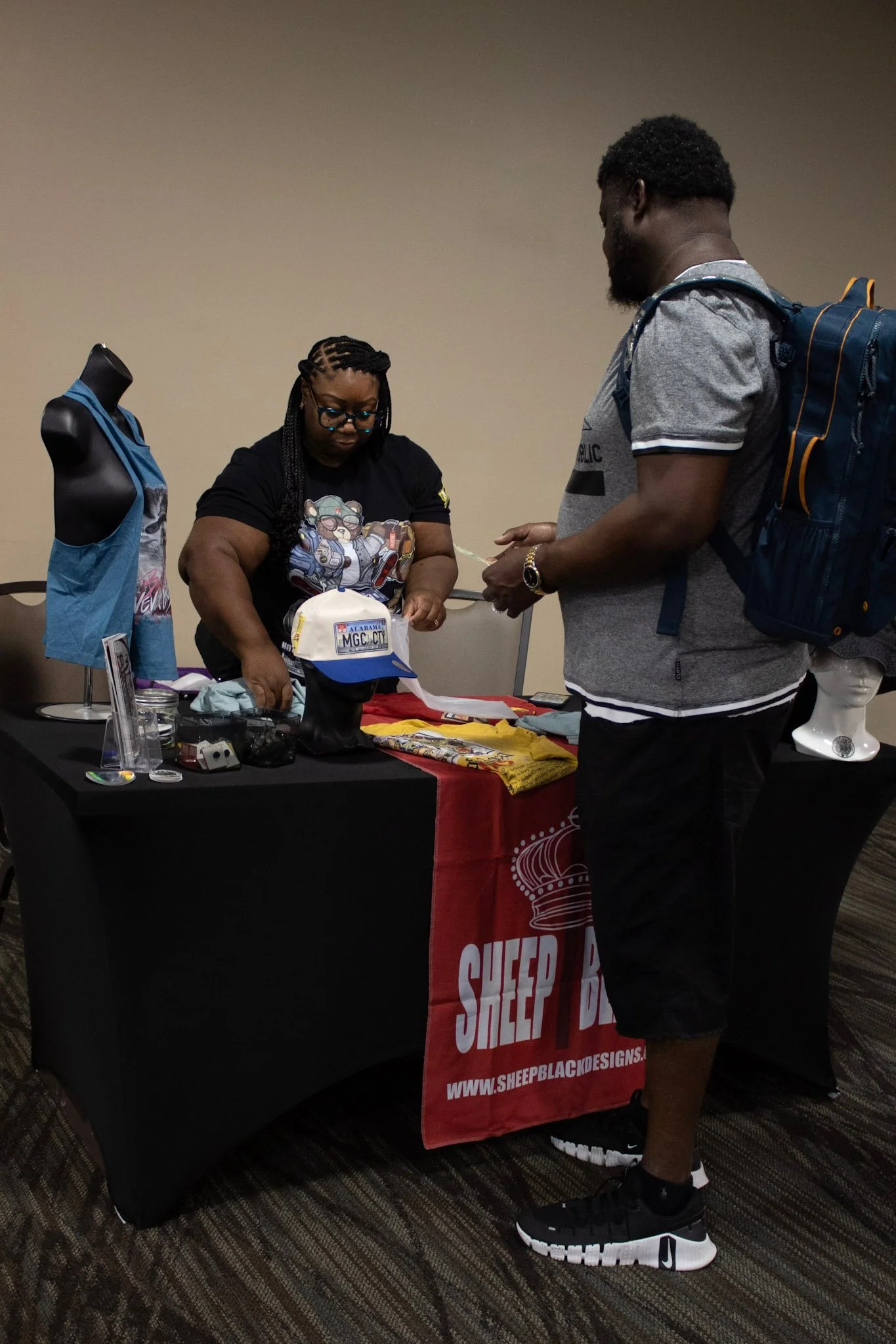 A woman and a man are at a booth displaying clothing and accessories, with the woman helping the man with purchase or inquiries.