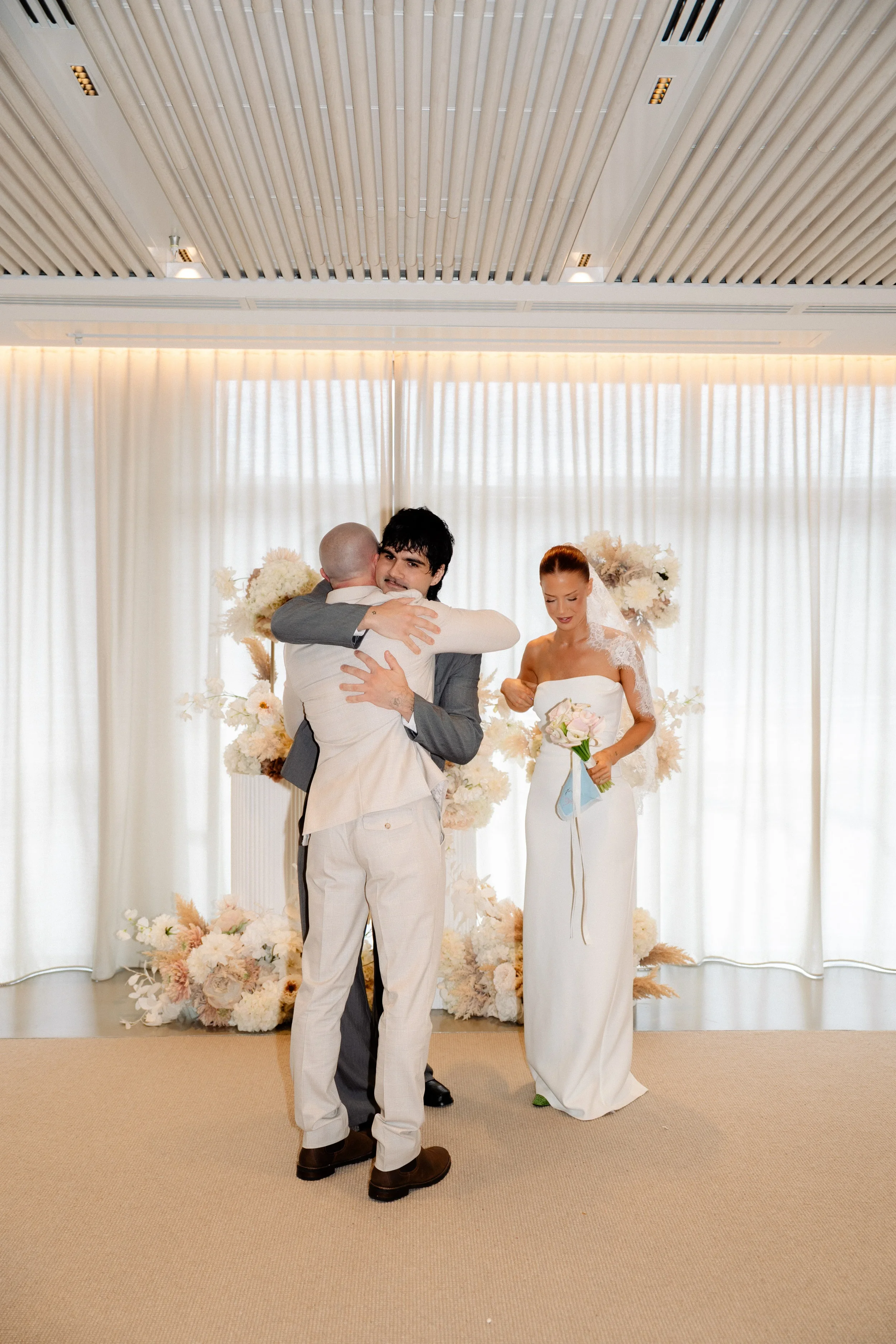 Groom hugging a guest while the bride stands nearby during the ceremony