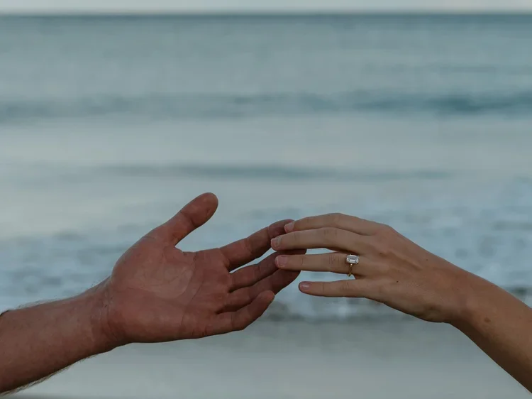 A couple holding hands on the beach, with the ocean waves in the background.