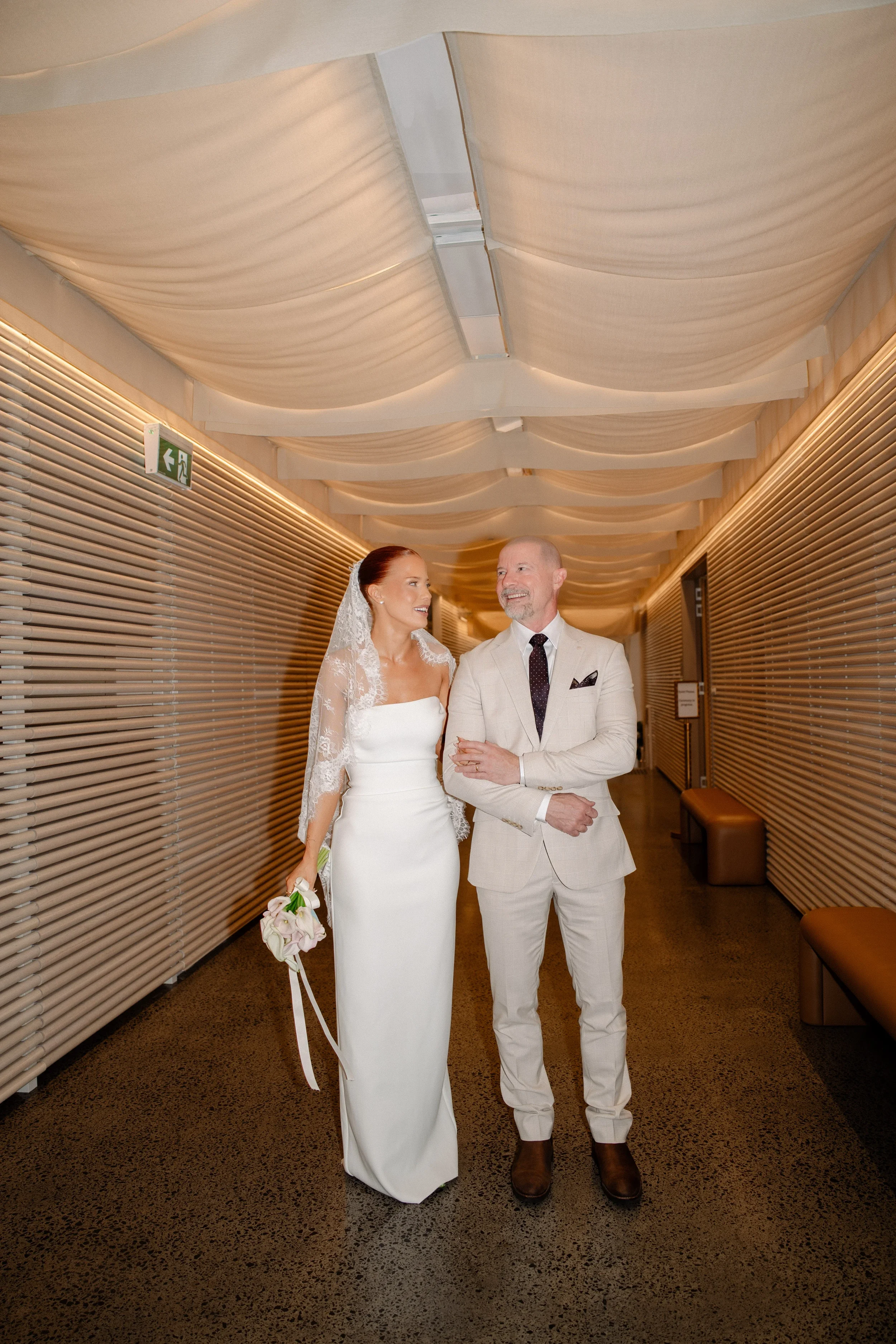 Bride walking with her father down a hallway before the ceremony