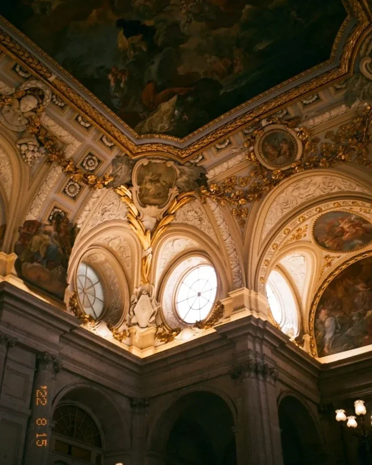 Ornate ceiling with gold accents, large windows, and intricate frescoes in a historic building.