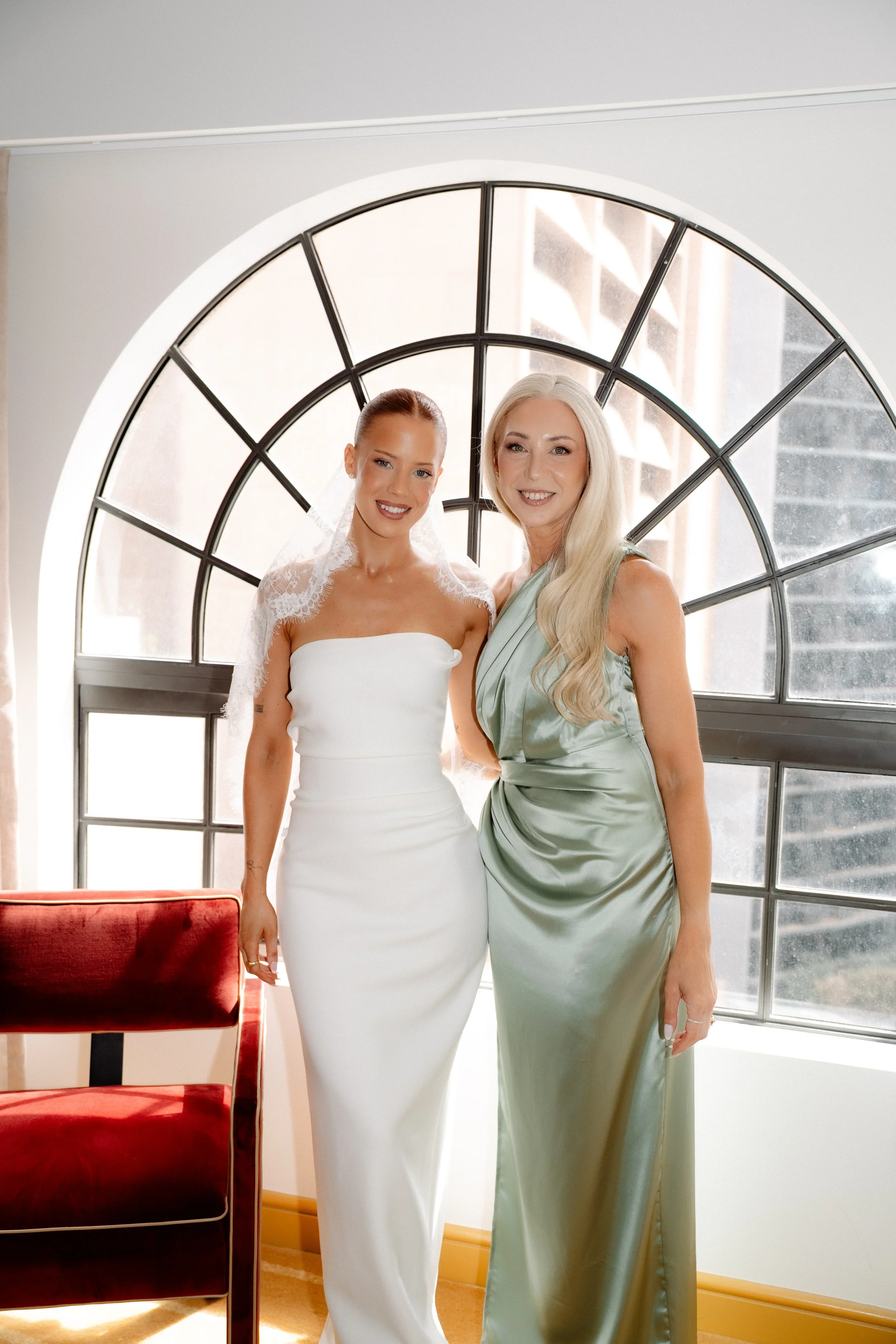 Bride posing with a bridesmaid by the arched window in natural light