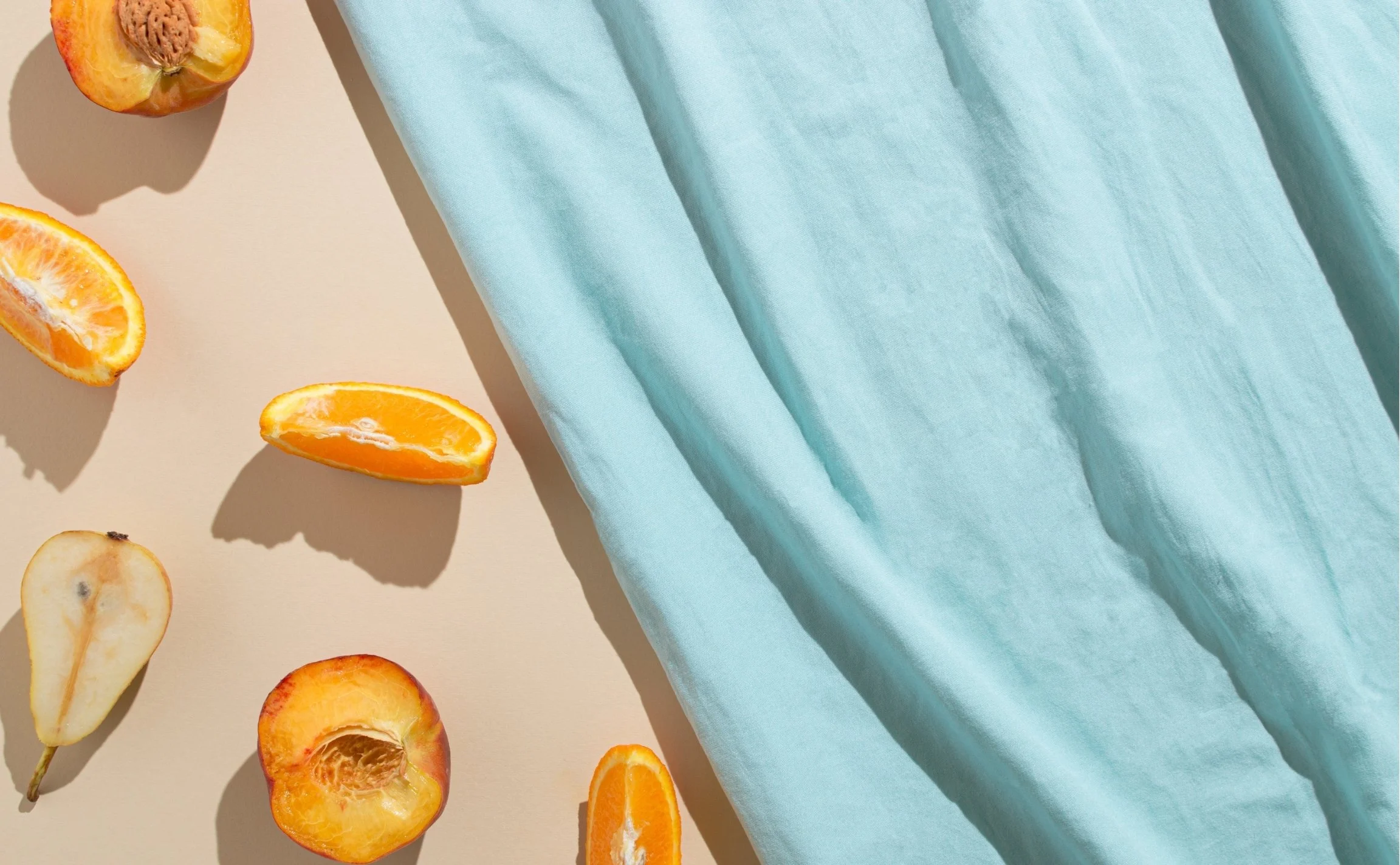 Various sliced fruits including peach, orange, pear, and apple arranged on a light surface, partially covered by a light blue fabric.