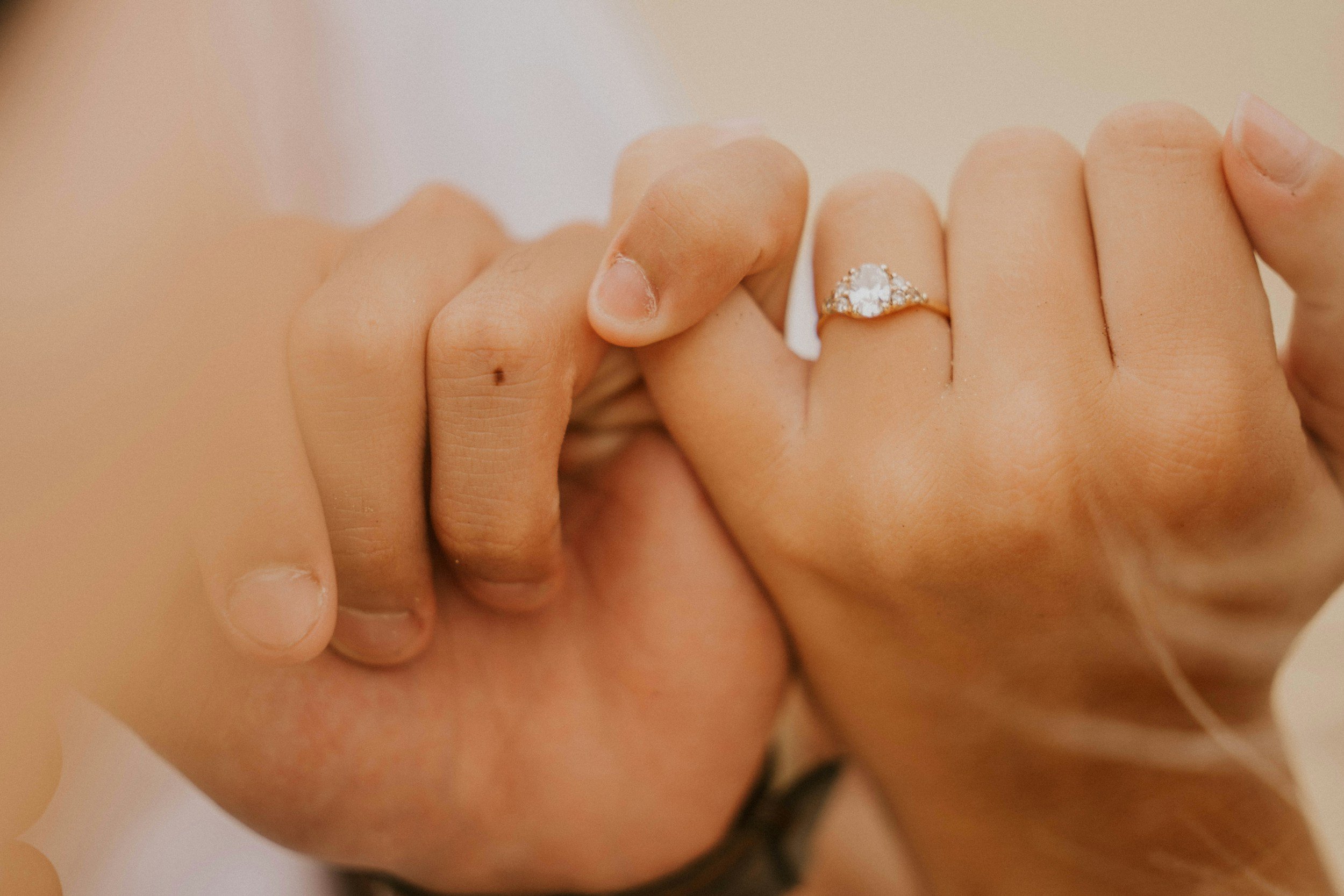 Close-up of a hand with a diamond engagement ring on the ring finger, touching a person's face.