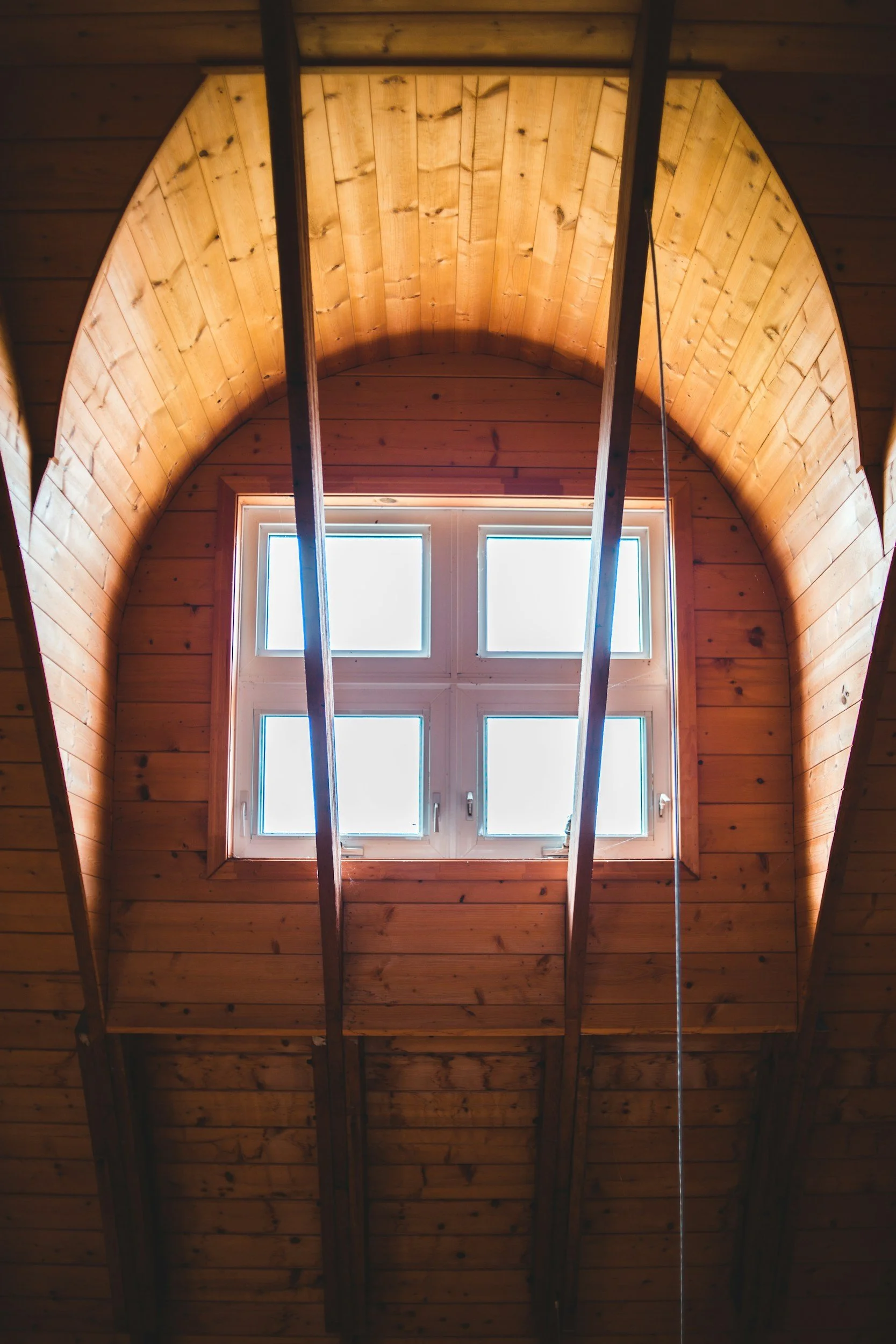 Interior view of a wooden ceiling with a large skylight window, showing natural light streaming in.