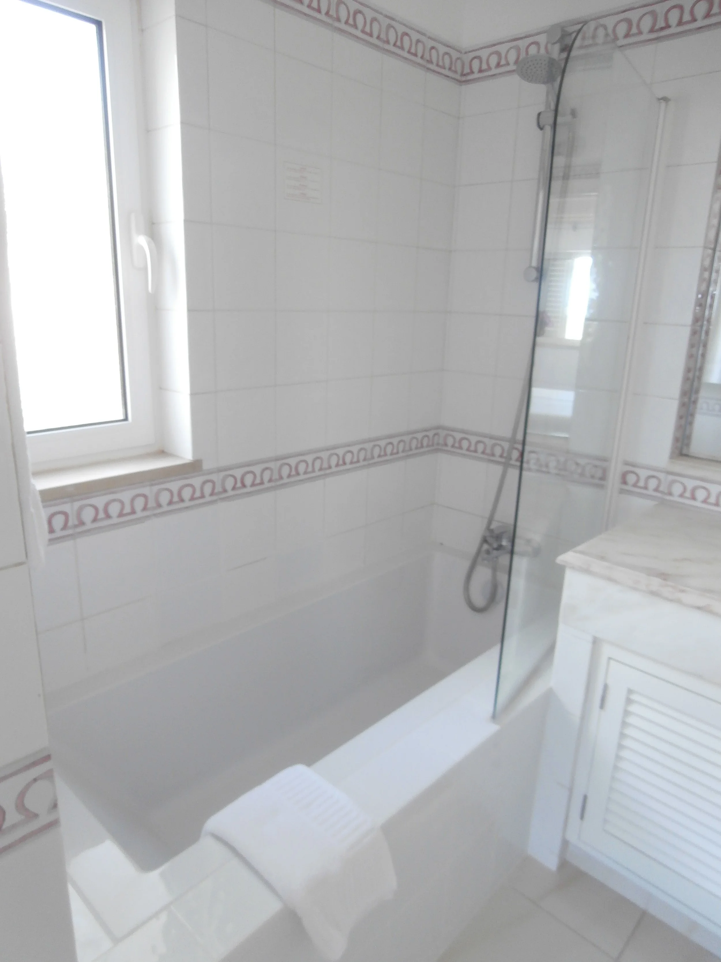 Empty narrow room with white walls, gray flooring, a small window near the ceiling, and a black object on the floor.