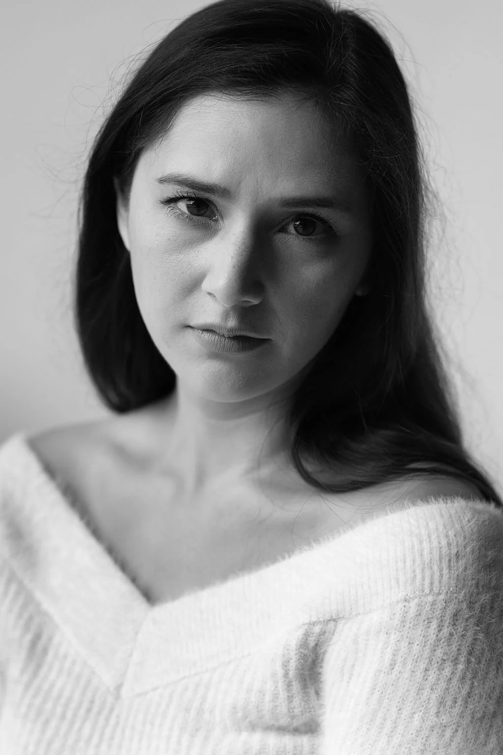 Black and white close-up portrait of a woman with dark hair, wearing a soft, textured sweater, looking directly at the camera with a serious expression.