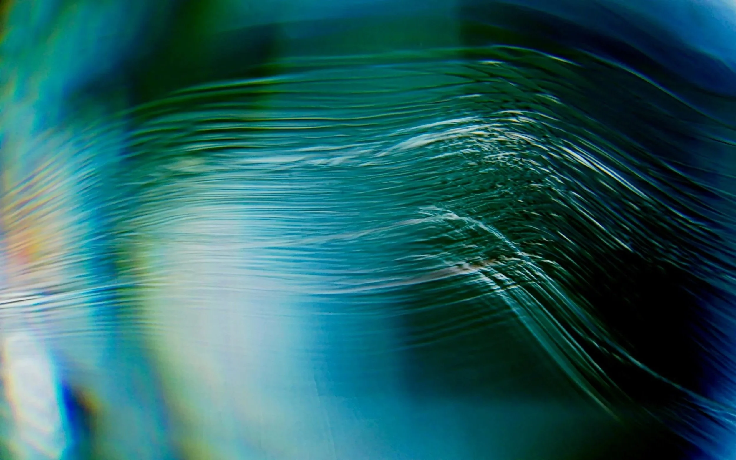 Close-up of a curling ocean wave with shades of blue, green, and hints of yellow along the edges.