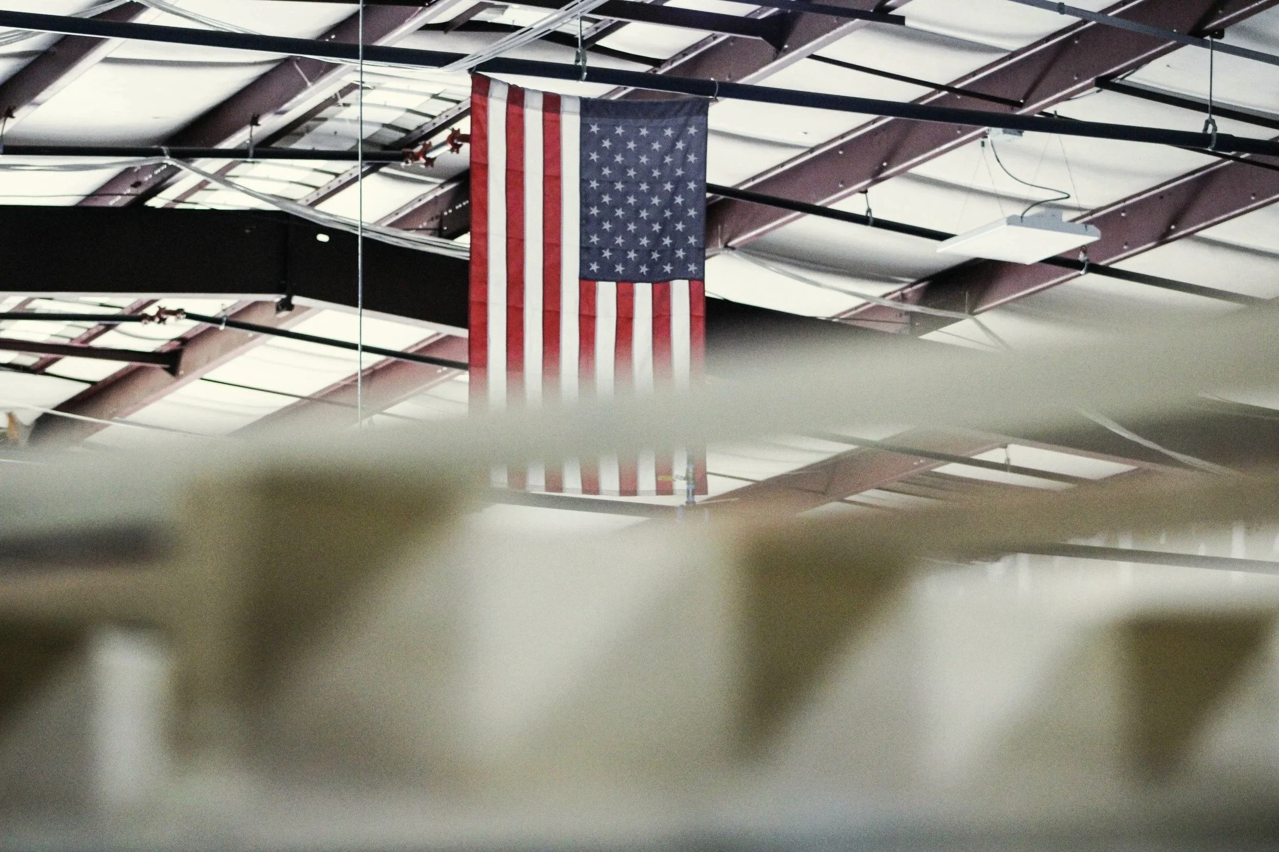 An American flag hanging from the ceiling of an indoor space with a metal roof and exposed beams.