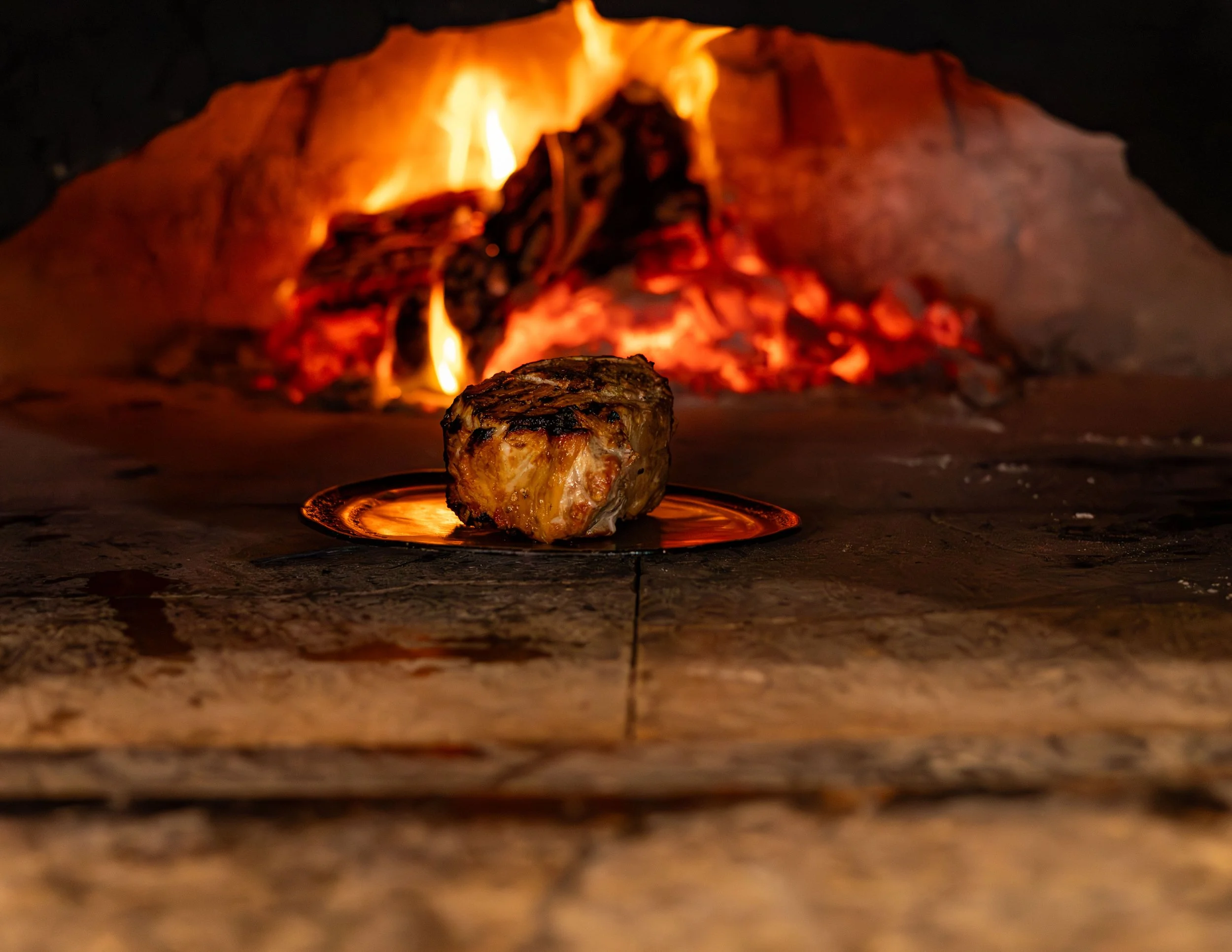 A piece of meat roasting on a spit over an open fire in a traditional brick oven.