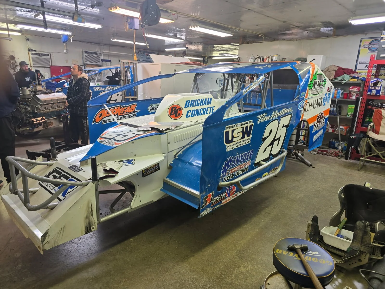 A race car with the number 25 and various sponsor logos on it, inside a garage with people working around it.