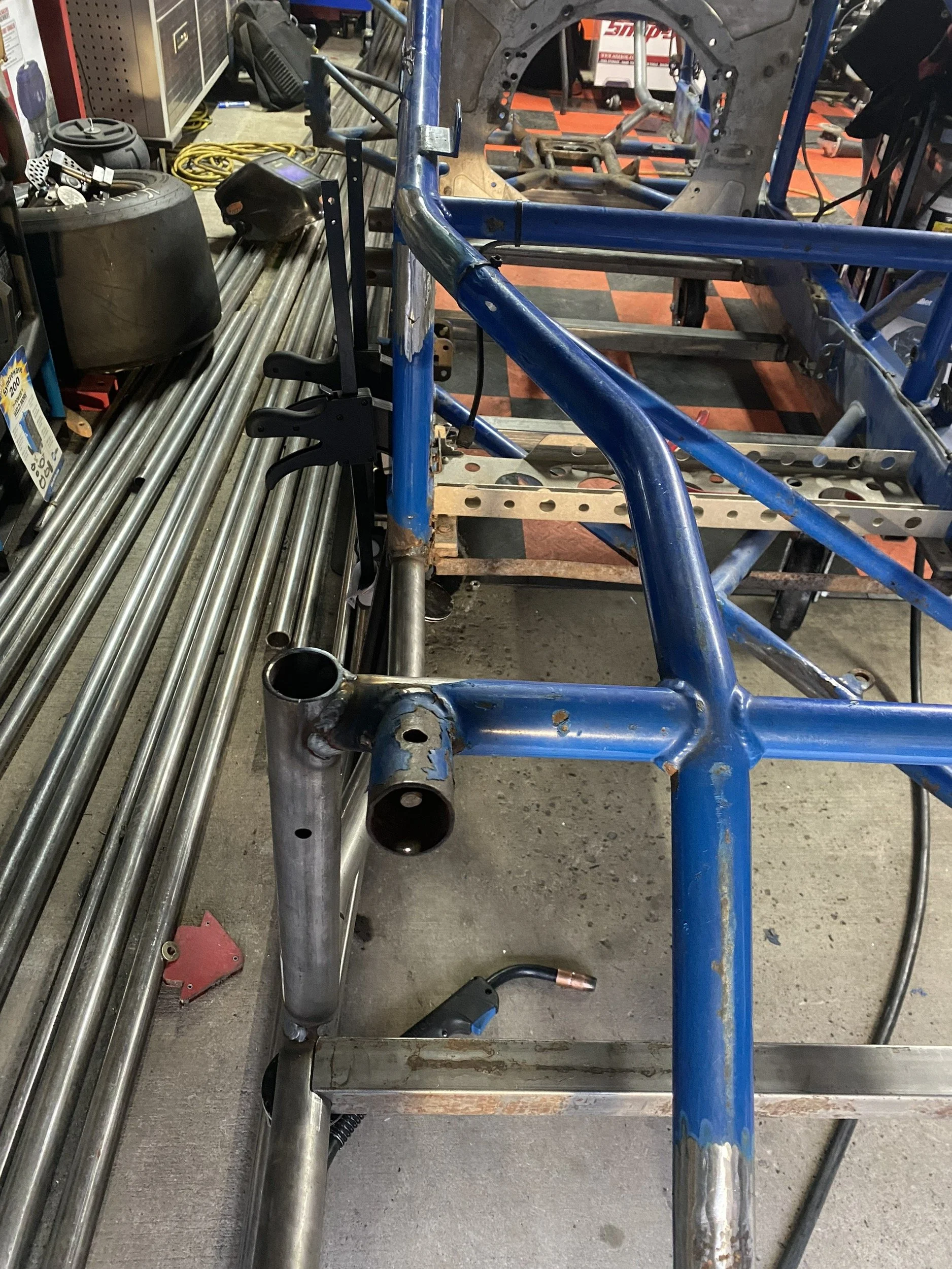 Car chassis frame in blue with some rust, on a metal worktable in a garage or workshop.