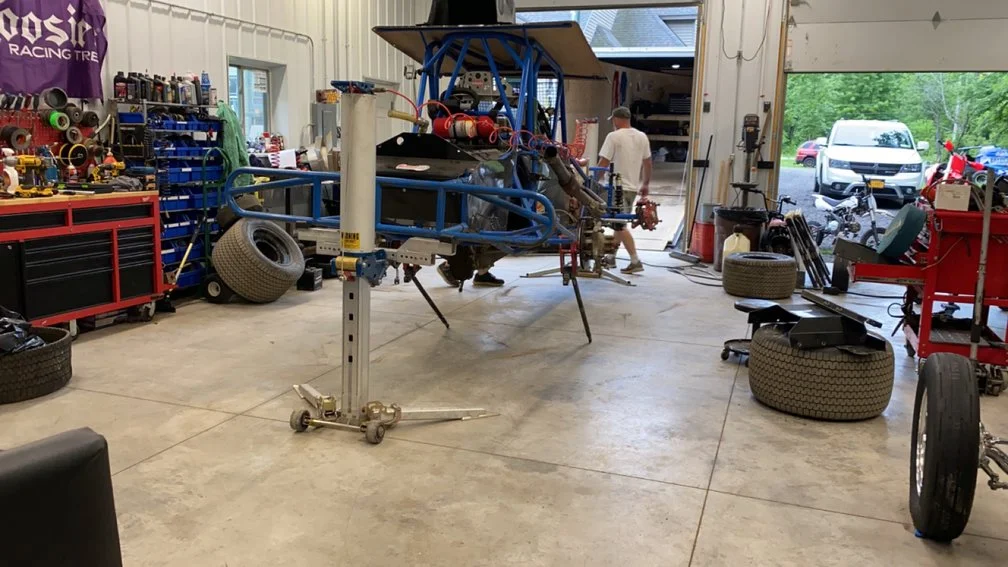 A race car being built inside a garage with tools, tires, and equipment around.