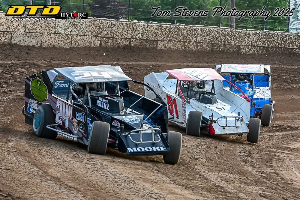 Three dirt track race cars on a dirt oval track, with the car numbered 24 in black and the car numbered 51 in white, racing closely together.