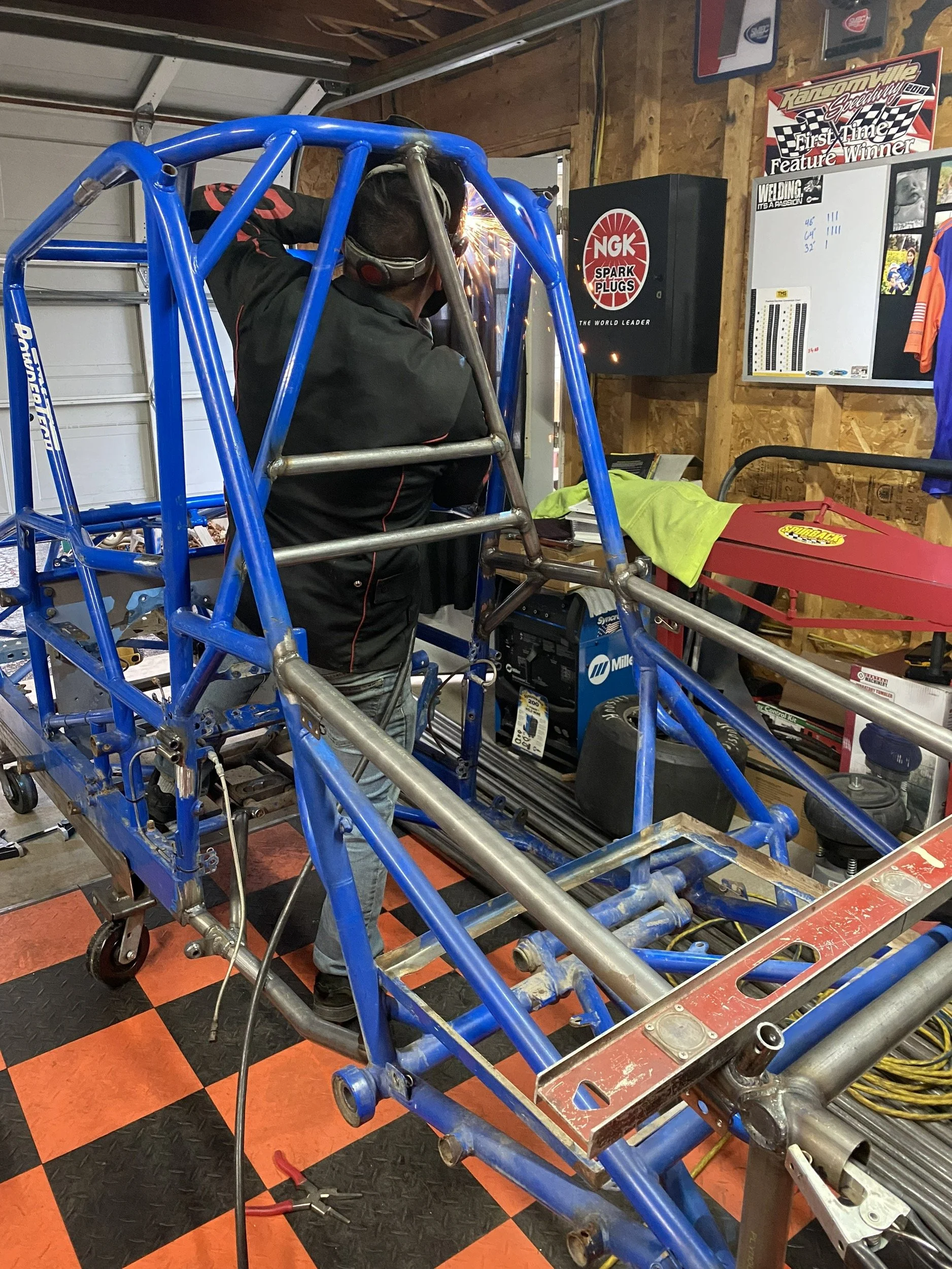 A person welding the frame of a blue race car inside a workshop.