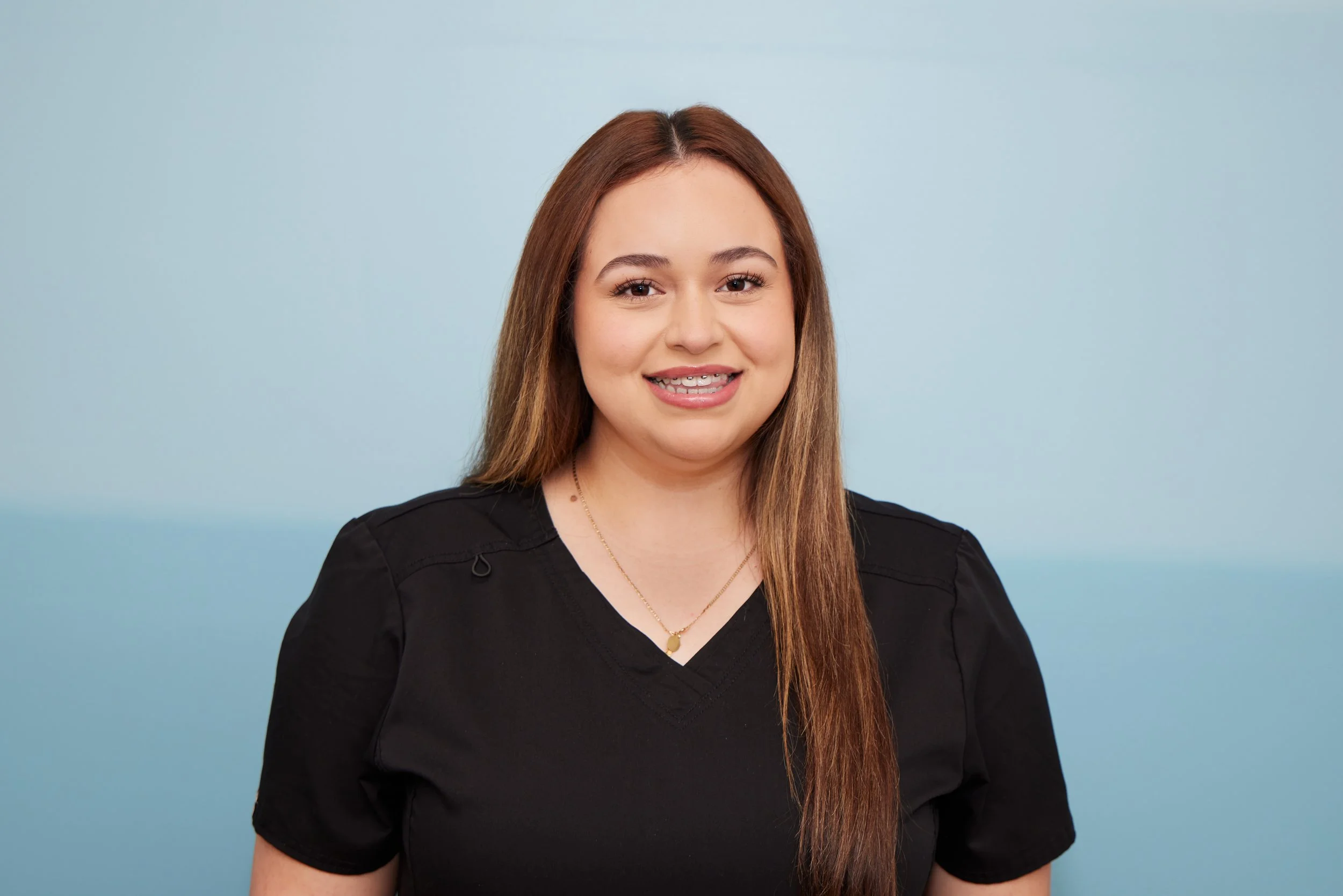 Young woman with brown hair and braces smiling in front of a blue background.