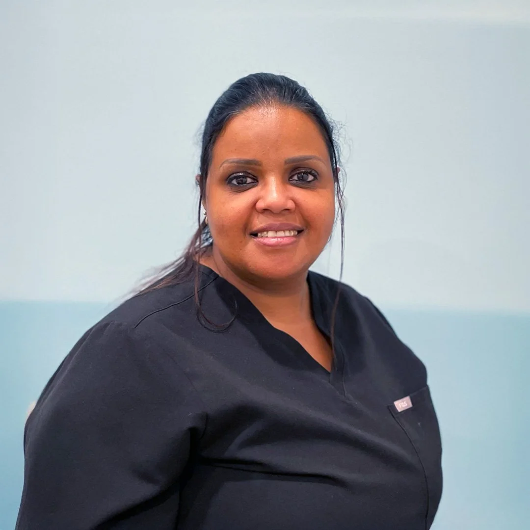 A woman in a black medical uniform smiling against a light blue background.