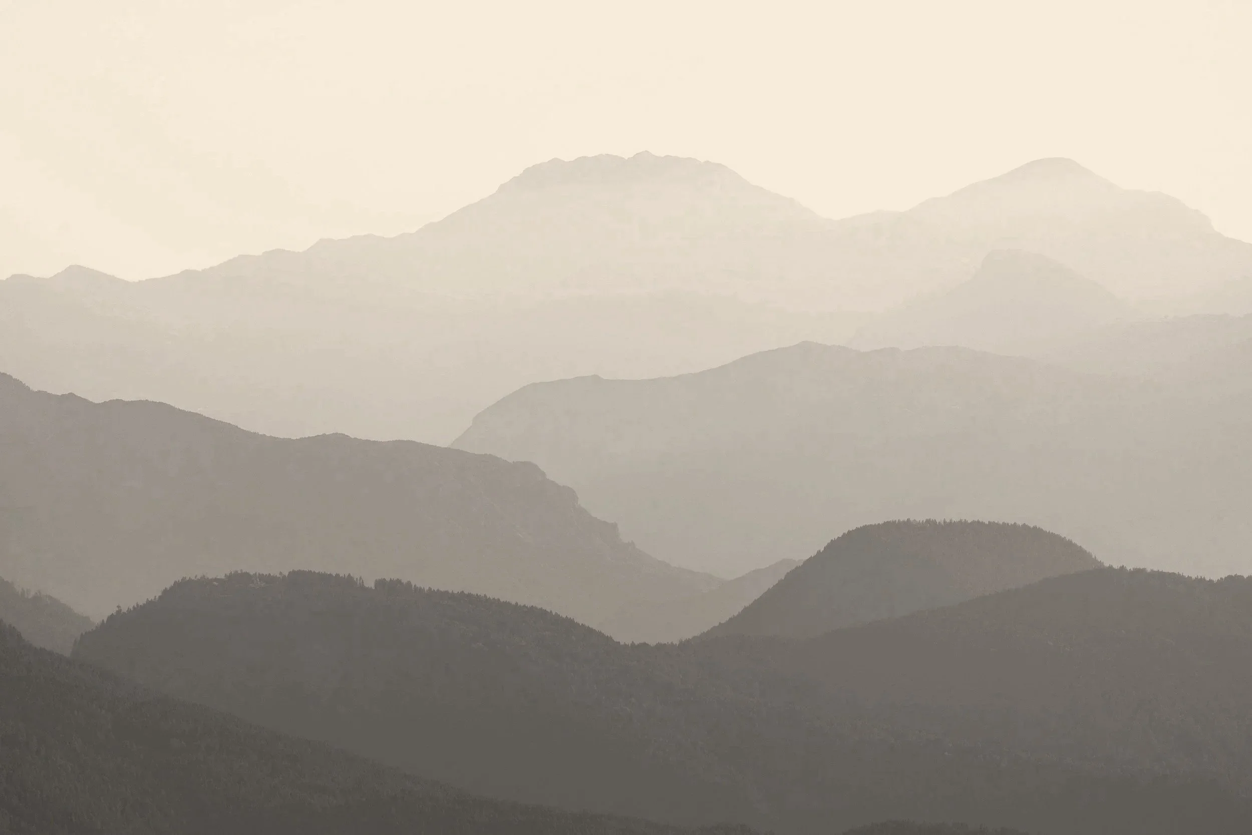 A landscape of multiple mountain ranges in muted shades of gray and beige, with mist or fog creating a layered, atmospheric effect.