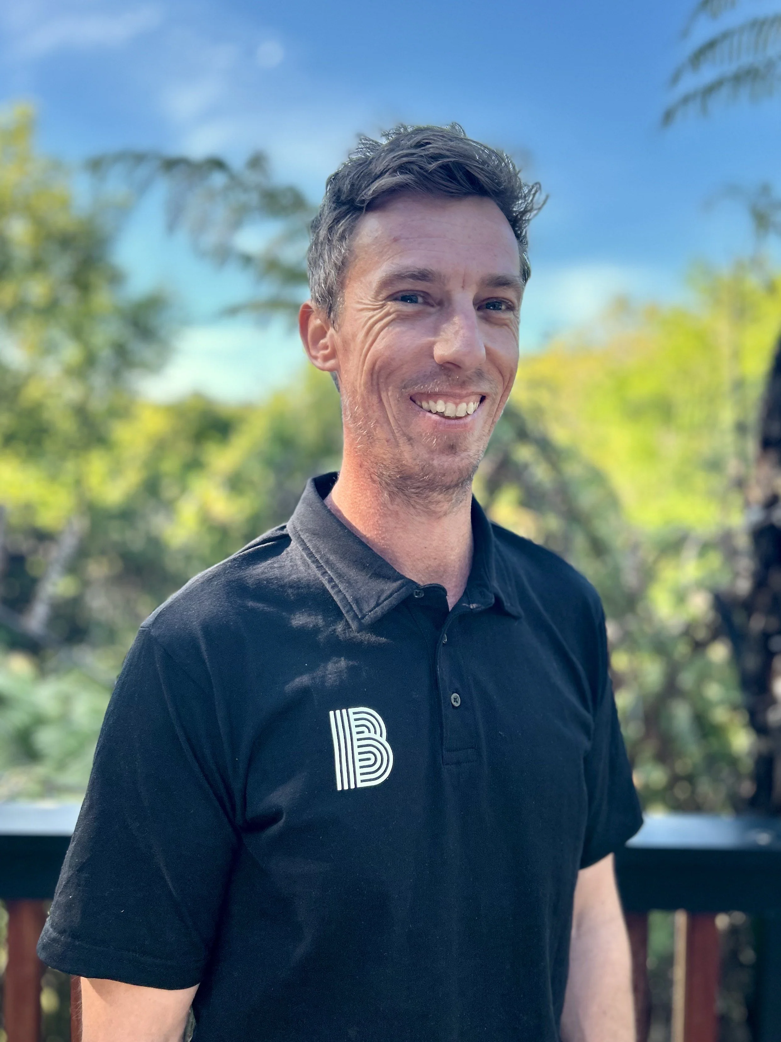 Image of Bayside Roofing owner and operator Matt Whitburn. Pictured in black shirt with Bayside Roofing logo, with sky and trees in background.