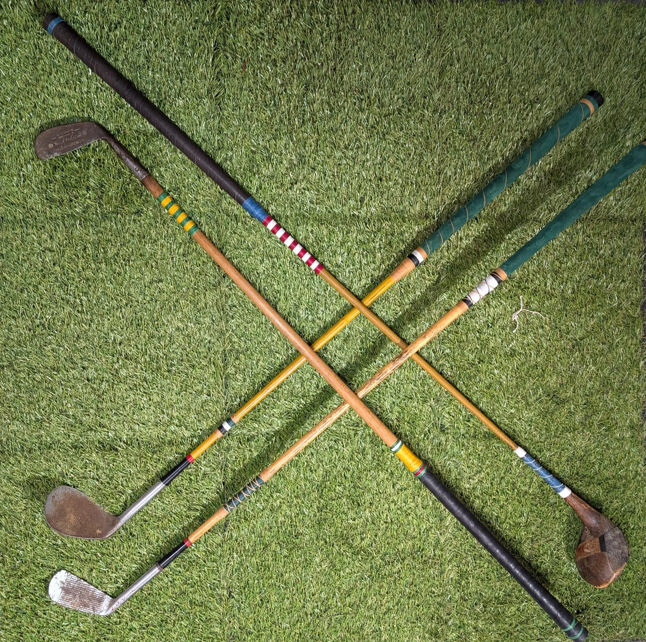 Four customized restored antique golf clubs crossed on a grassy background.