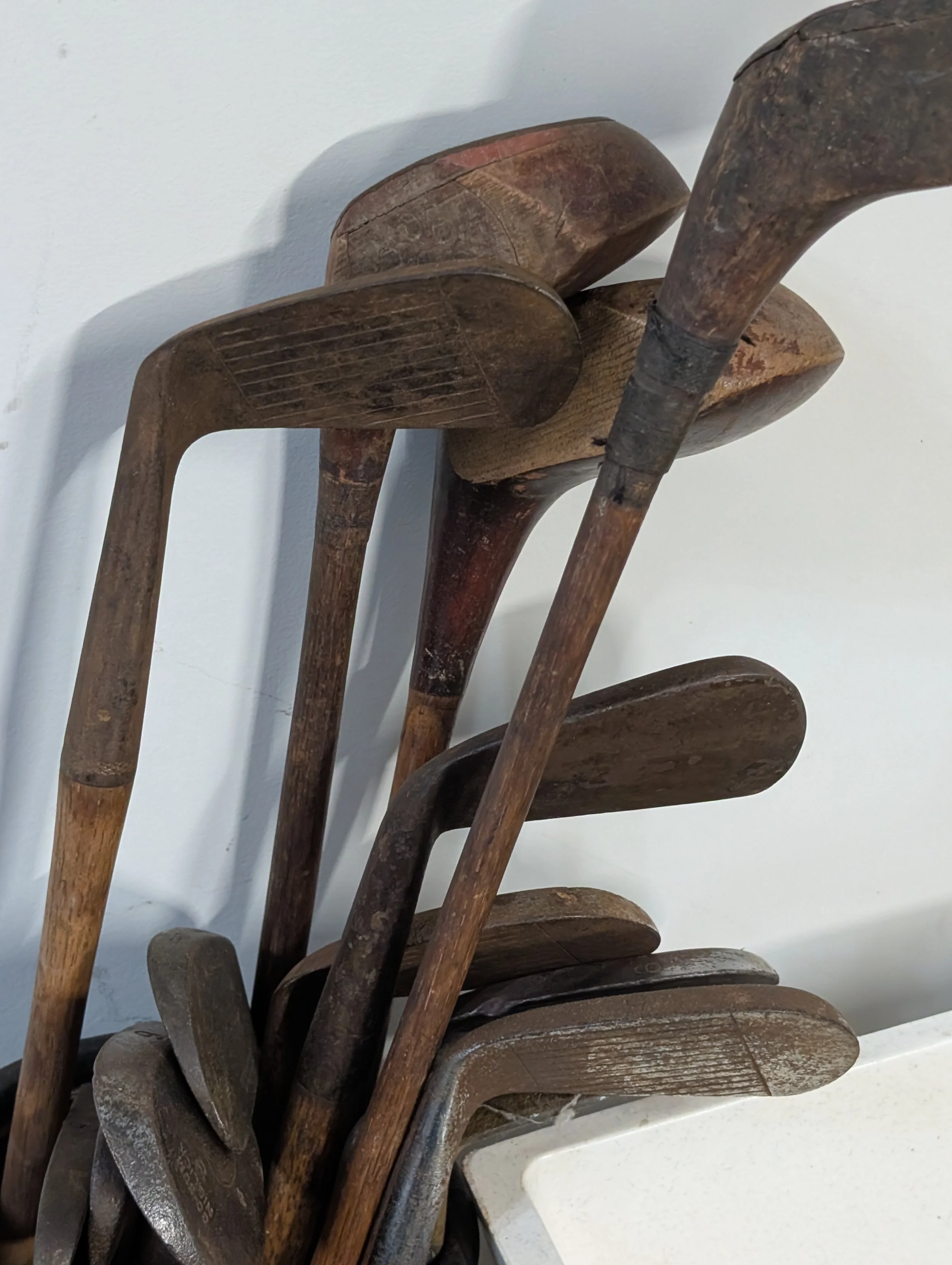A stack of old, weathered hickory golf clubs leaning against a wall.