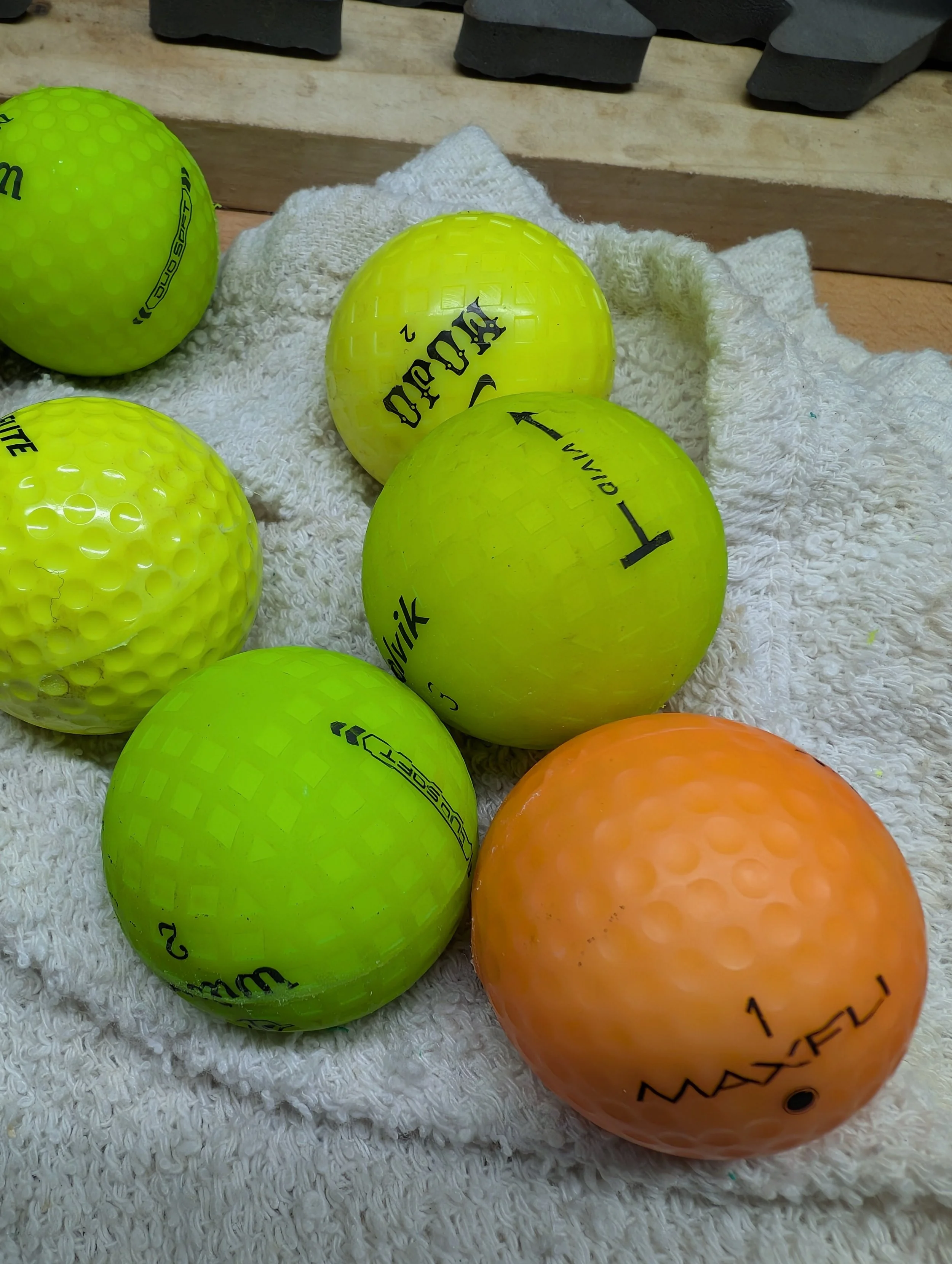 A collection of golf balls in bright colors including yellow, orange, and green, resting on a white towel on a wooden surface.