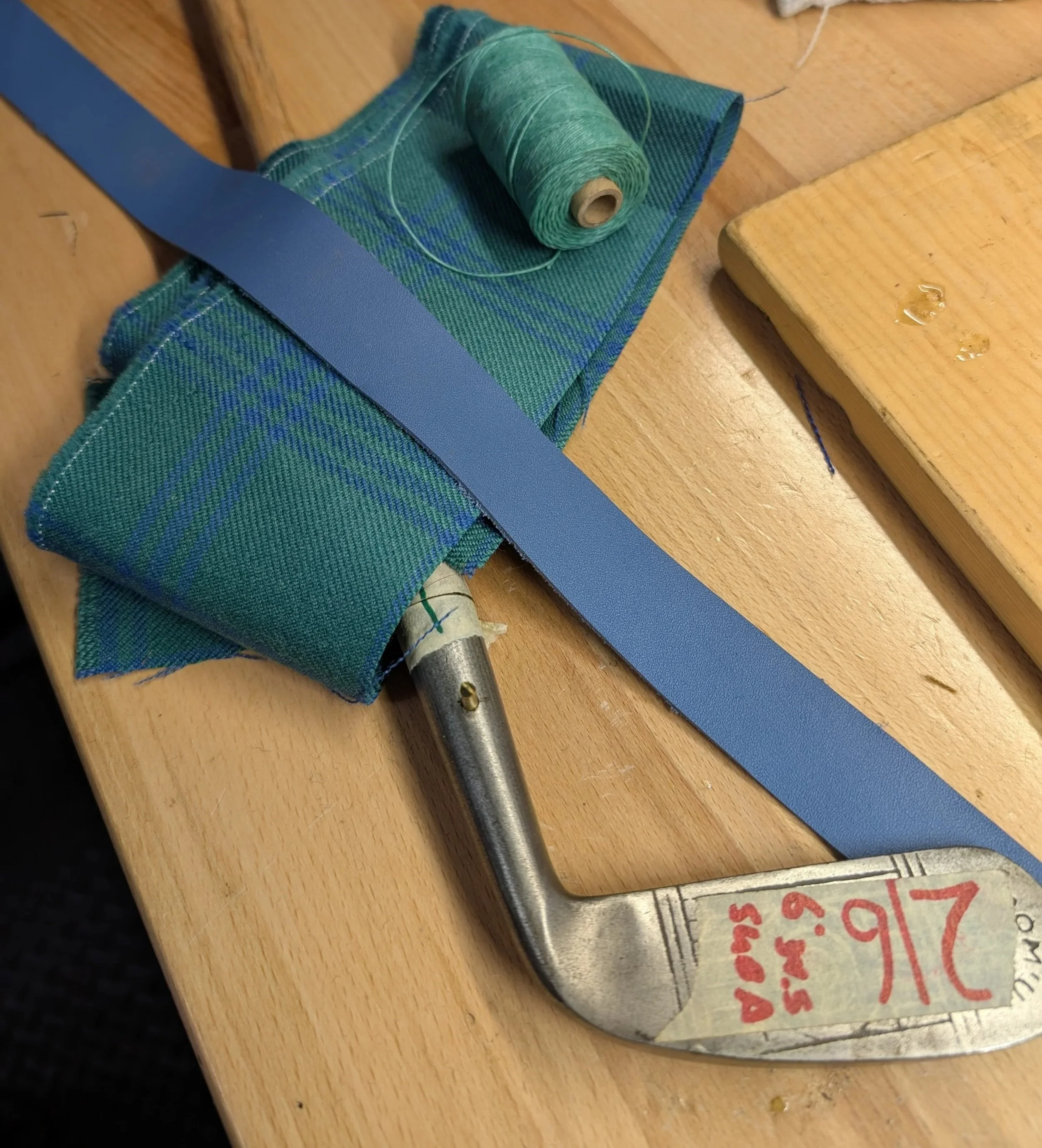A partially restored hickory golf club with leather, thread, and tartan fabric that will be used to complete the restoration.