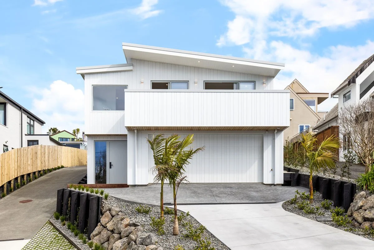 Modern coastal new build with white cladding, balcony, double garage, and landscaped driveway.