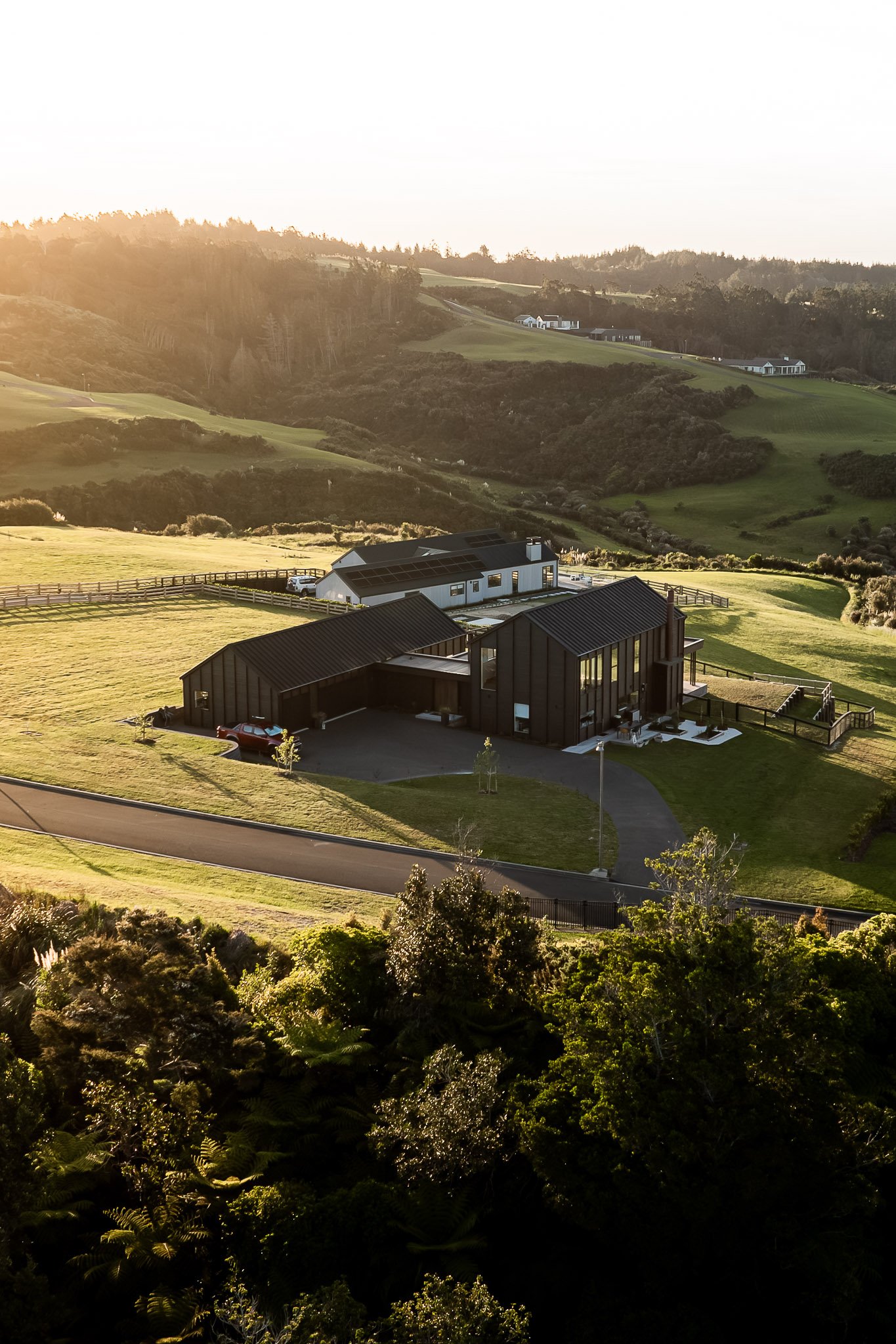 Front view of The Ridge with circular driveway, garage entry, and sweeping coastal-pastoral landscape at Weiti Bay.