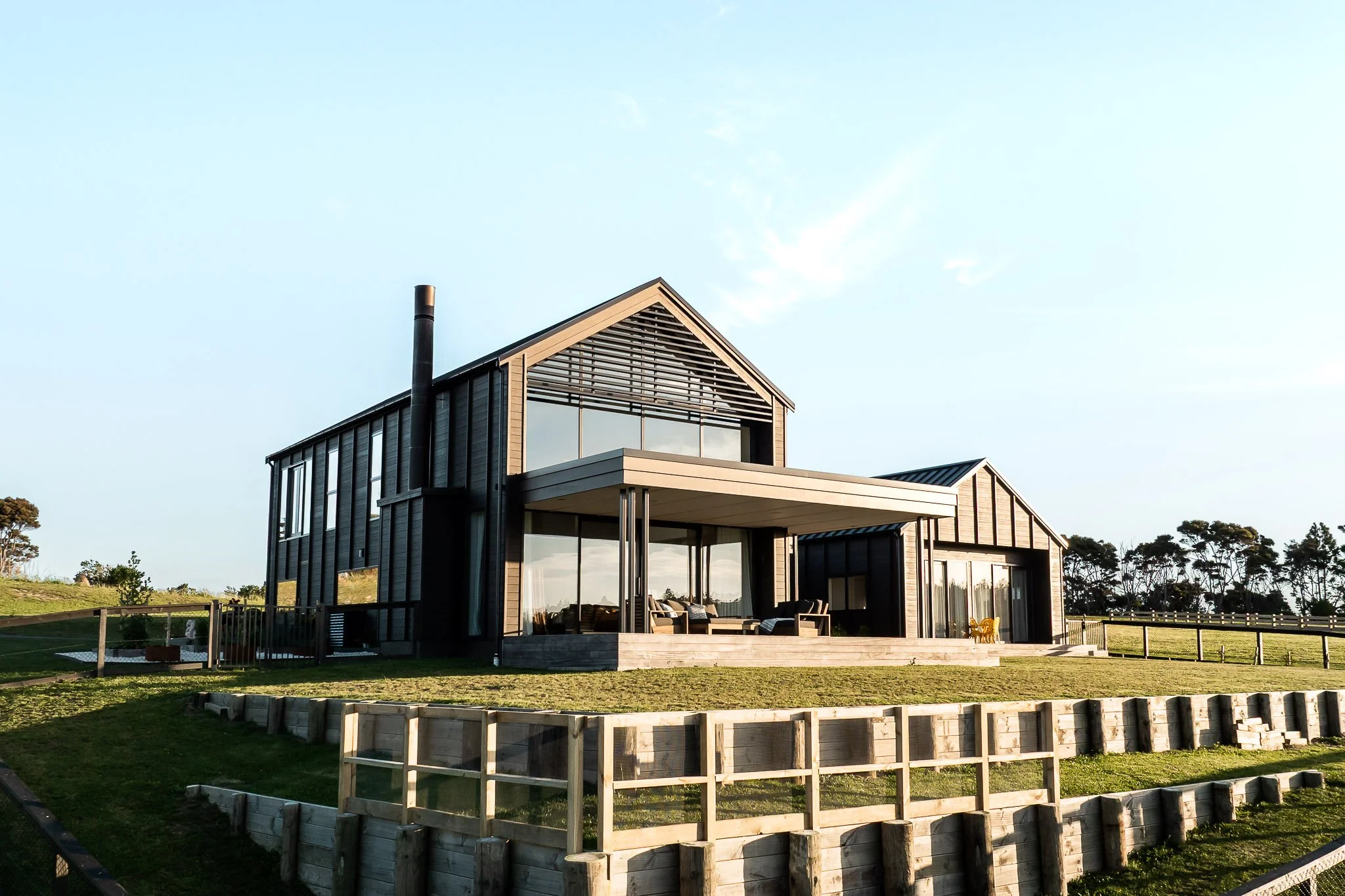 Architectural new build at Weiti Bay, featuring crisp board-and-batten weatherboard siding perched on a clifftop overlooking bushland and ocean.
