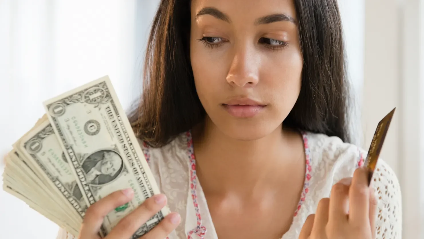 A young woman holding cash and a credit card, illustrating Gen Z financial independence and increased savings habits.