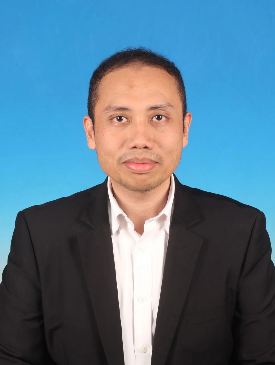 Professional portrait of a man wearing a black suit jacket and white shirt against a blue background.