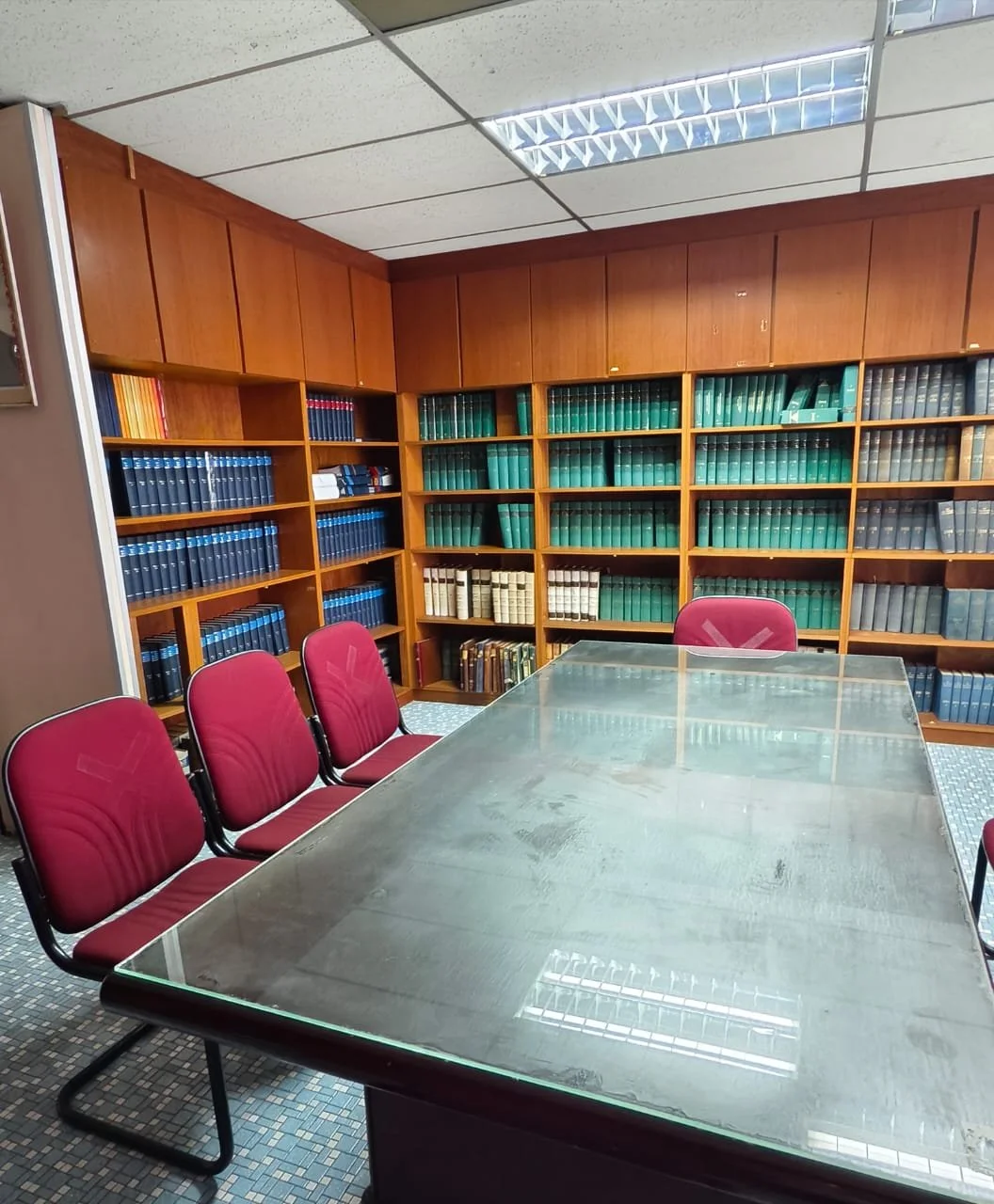A conference room with a glass table and red chairs. Wooden bookshelves filled with law books line the walls.