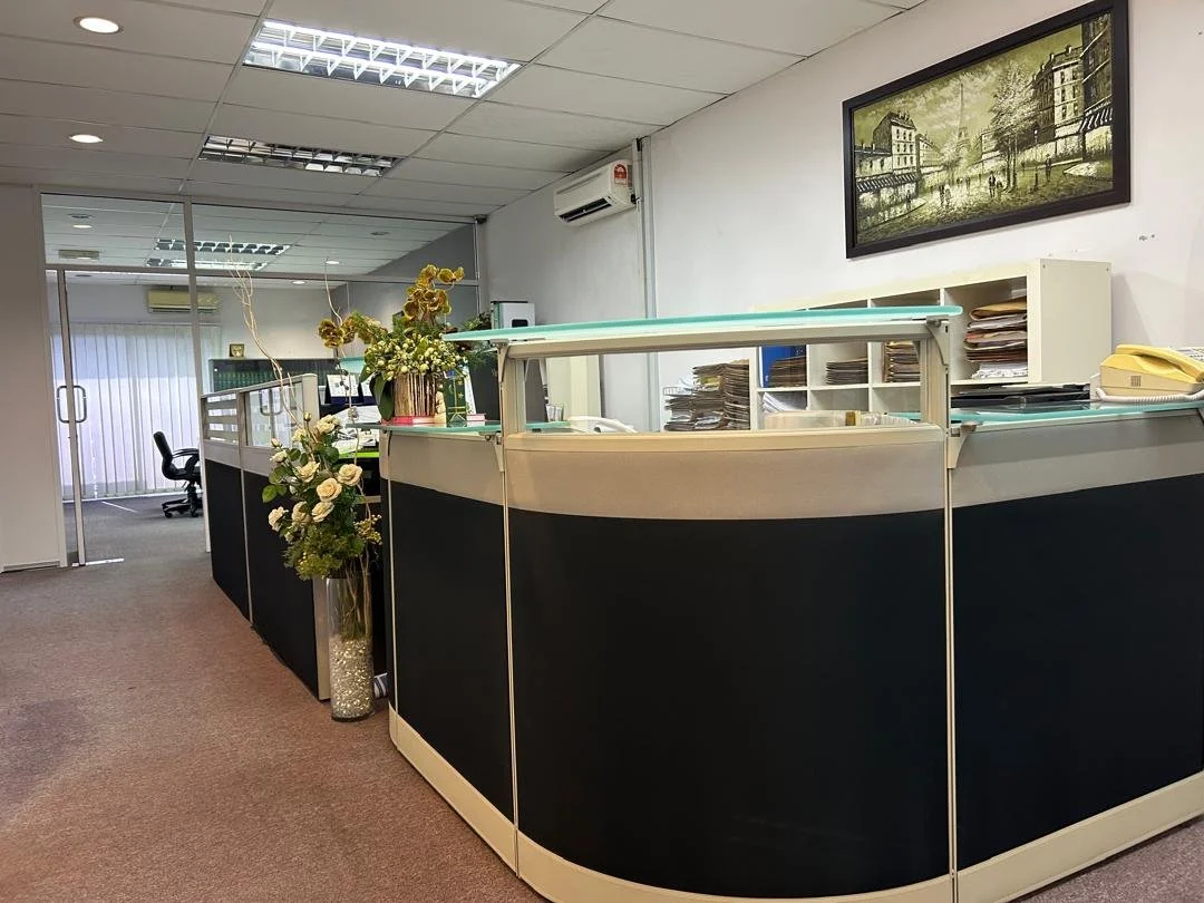 Office reception desk with flower arrangements, shelves with stacks of files, and framed artwork on the wall.