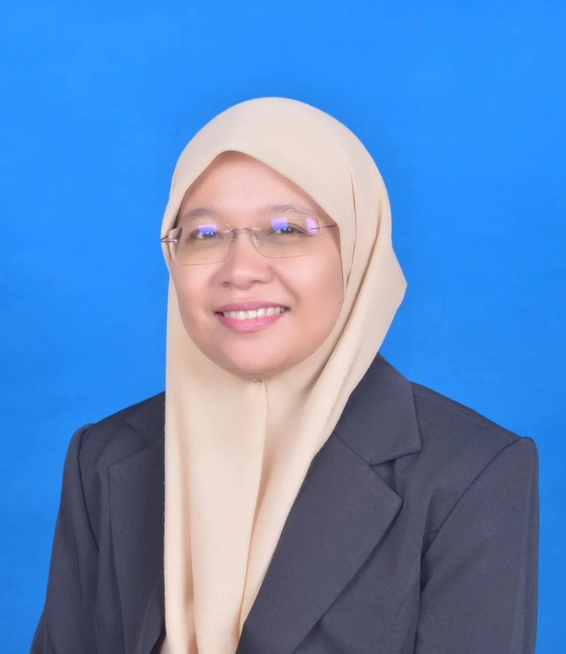 Professional woman wearing glasses and a beige hijab, smiling, against a solid blue background.