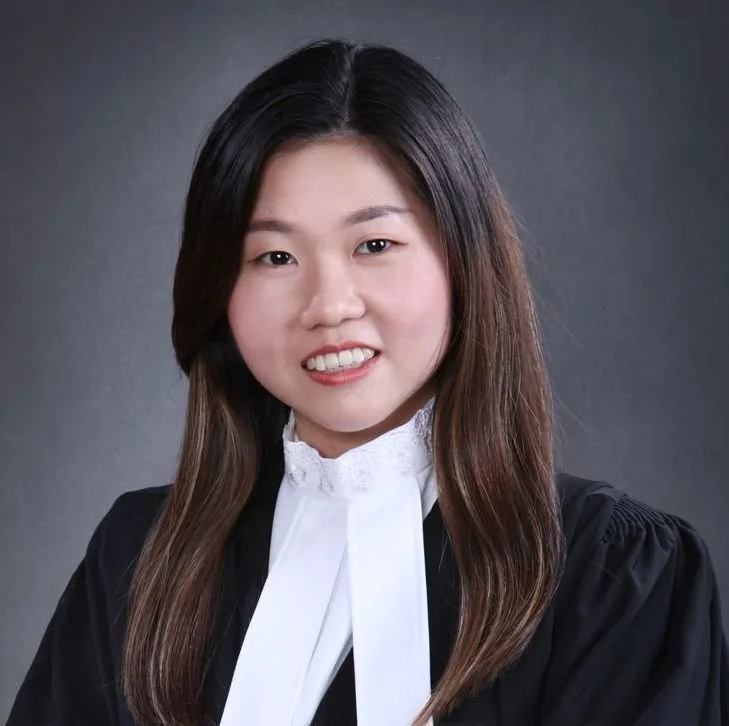 Professional woman in legal robe with white collar and black gown, smiling, against dark background.