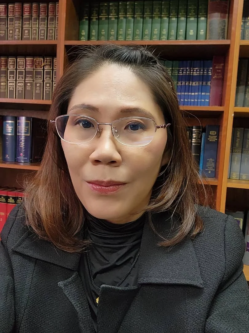 A woman in glasses and black clothing taking a selfie in front of a bookshelf filled with law books.