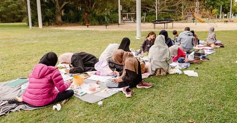 Group outdoor nature journaling workshop with participants drawing and painting together in a park setting.
