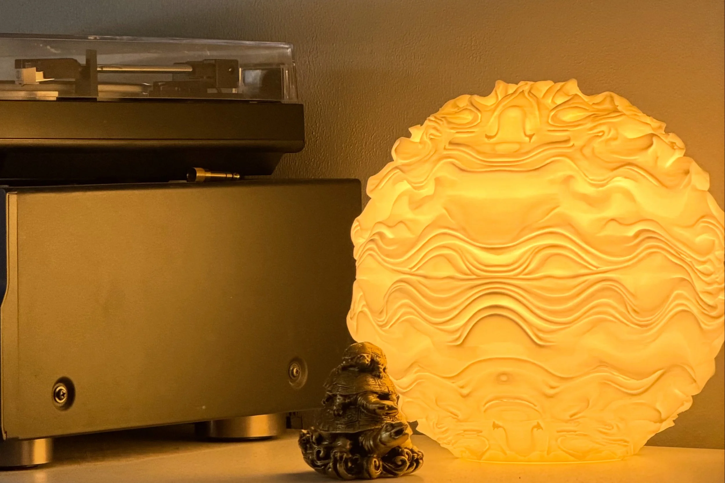A glowing, intricately textured lampshade with a swirling pattern on a surface, accompanied by a small decorative figure and electronic equipment.