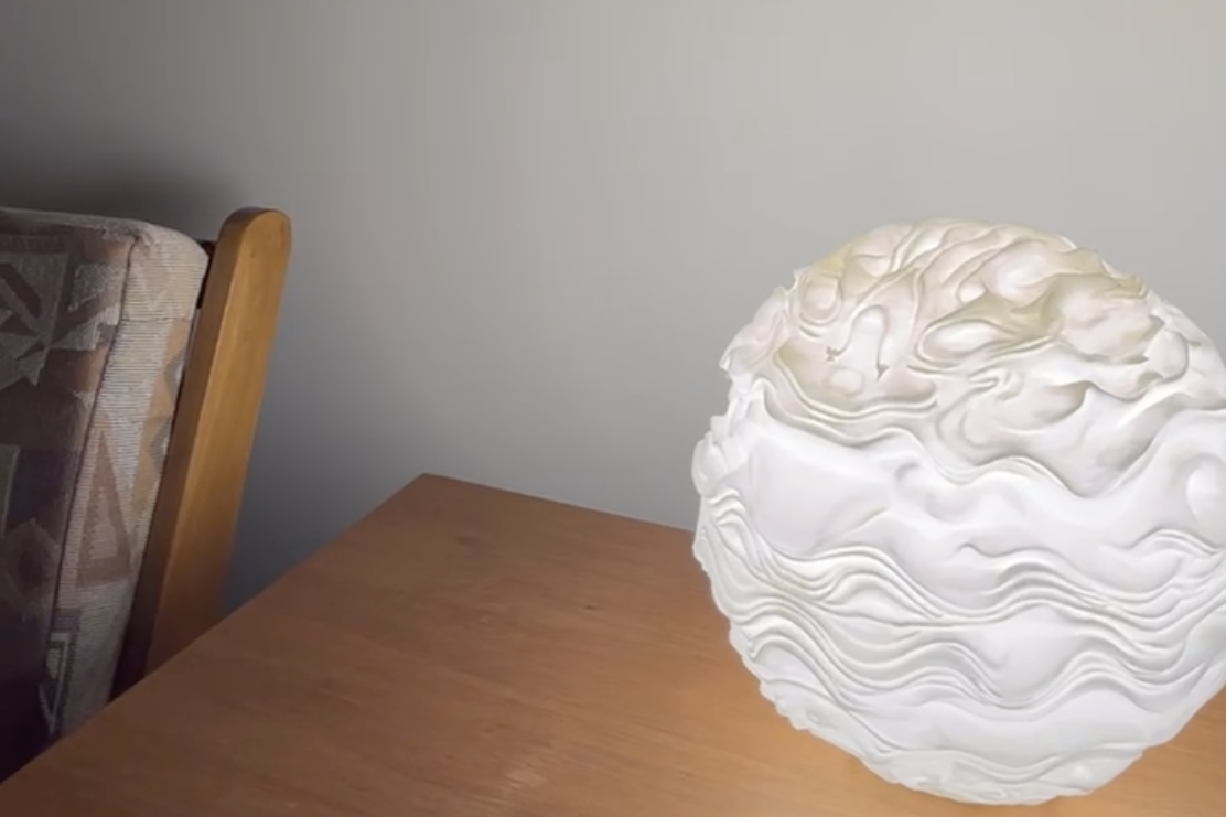 Close-up of a white, textured paper lantern on a wooden table, with a part of a patterned upholstered chair visible in the background.