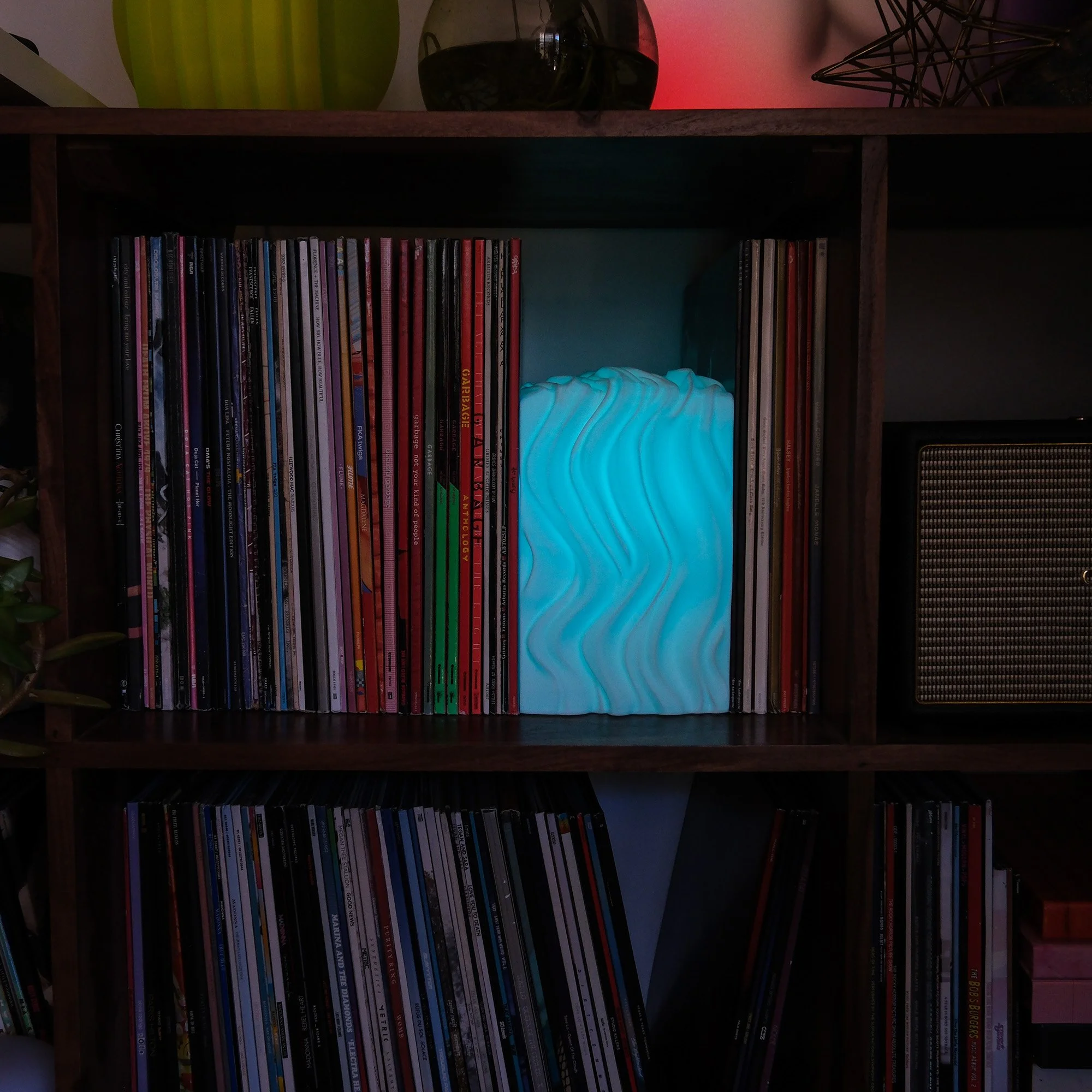A wooden bookshelf filled with vinyl records and a glowing blue decorative lamp with wavy patterns.