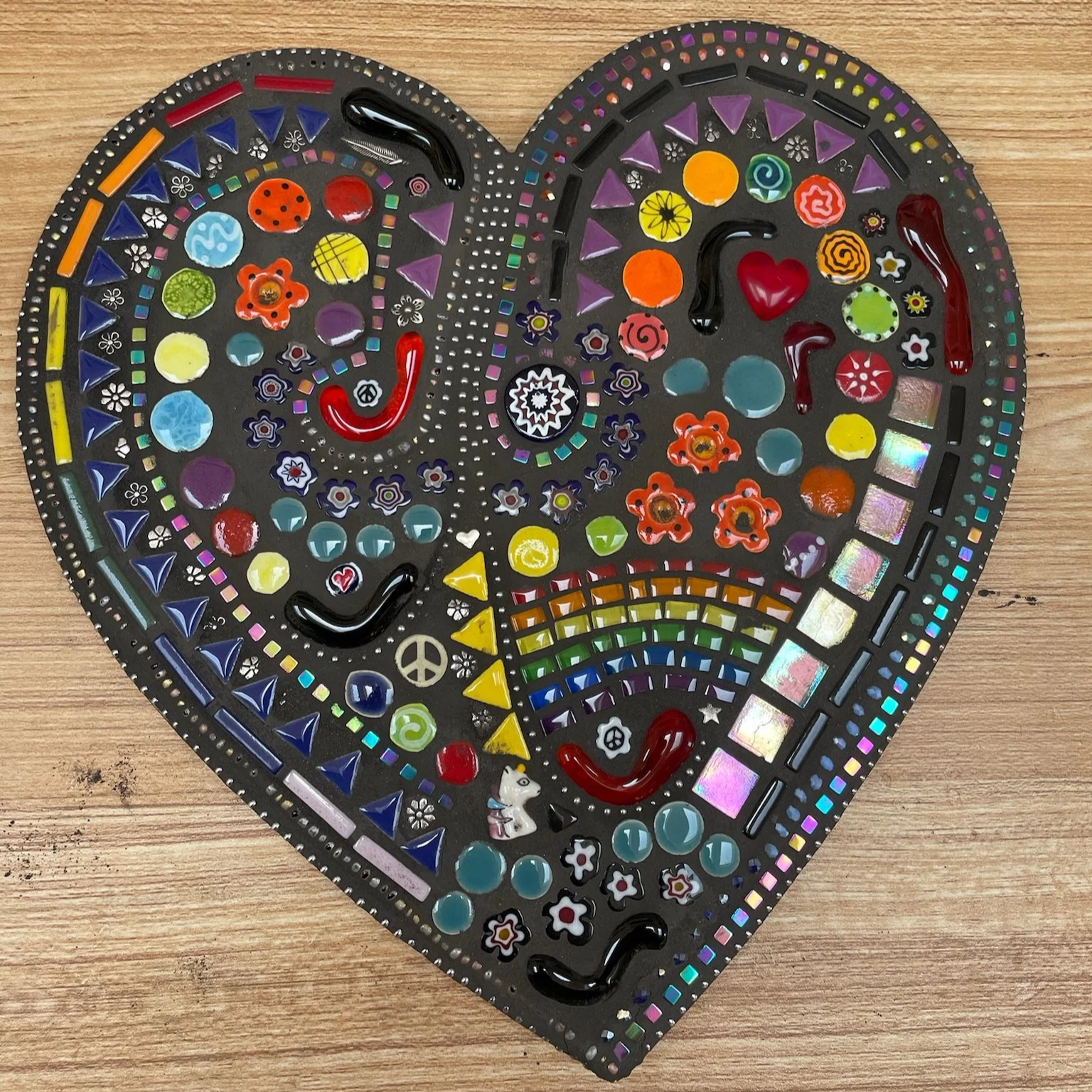 Decorative mosaic heart artwork with colorful glass pieces, beads, and embellishments on a wooden surface.