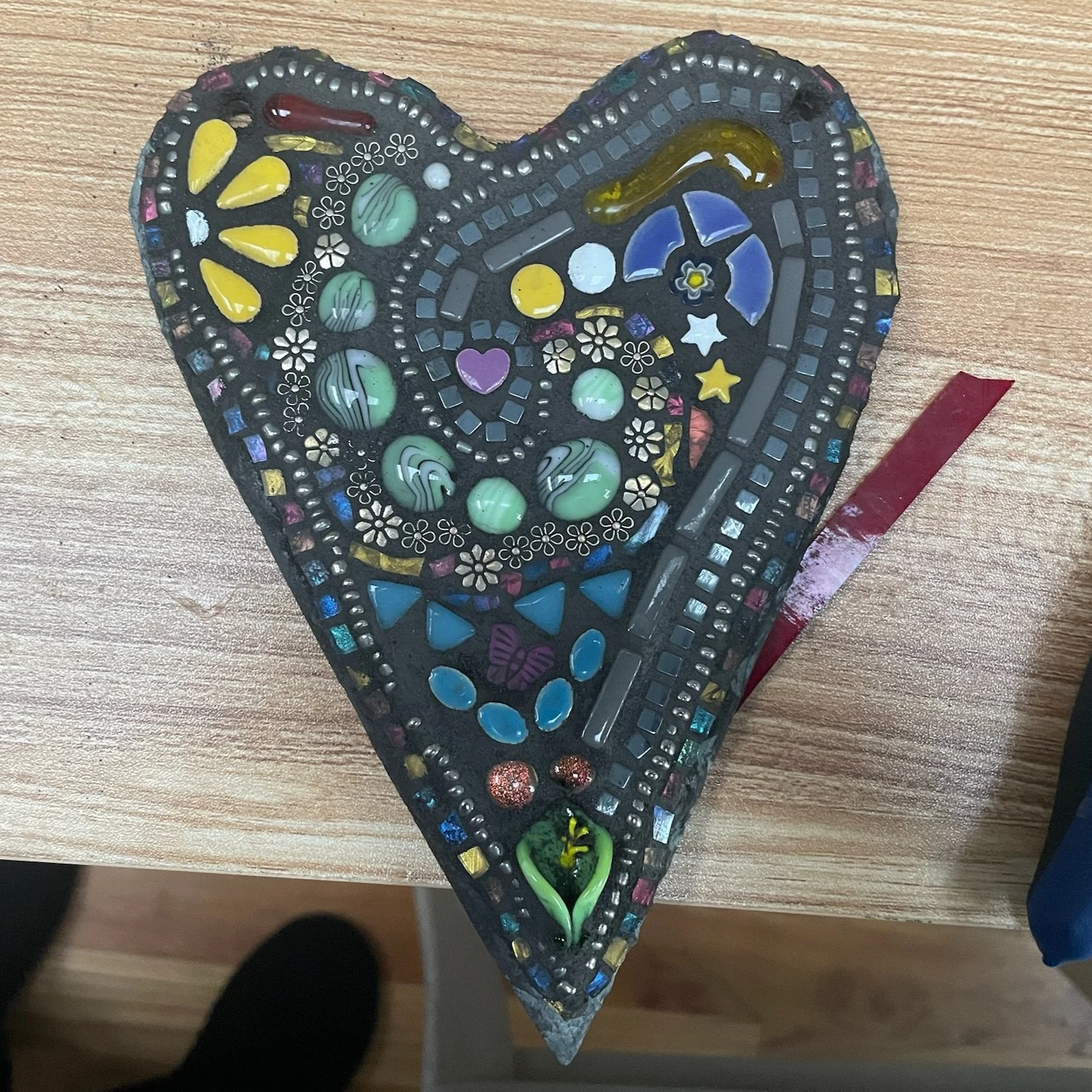 A colorful mosaic heart made of small glass and ceramic pieces on a wooden surface.