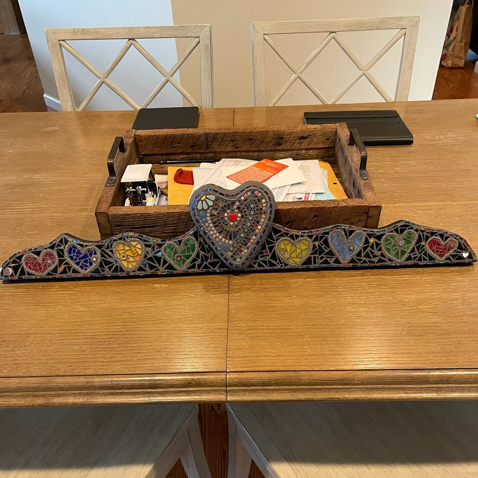 Decorative mosaic heart and rainbow hearts on a black base on a wooden dining table.