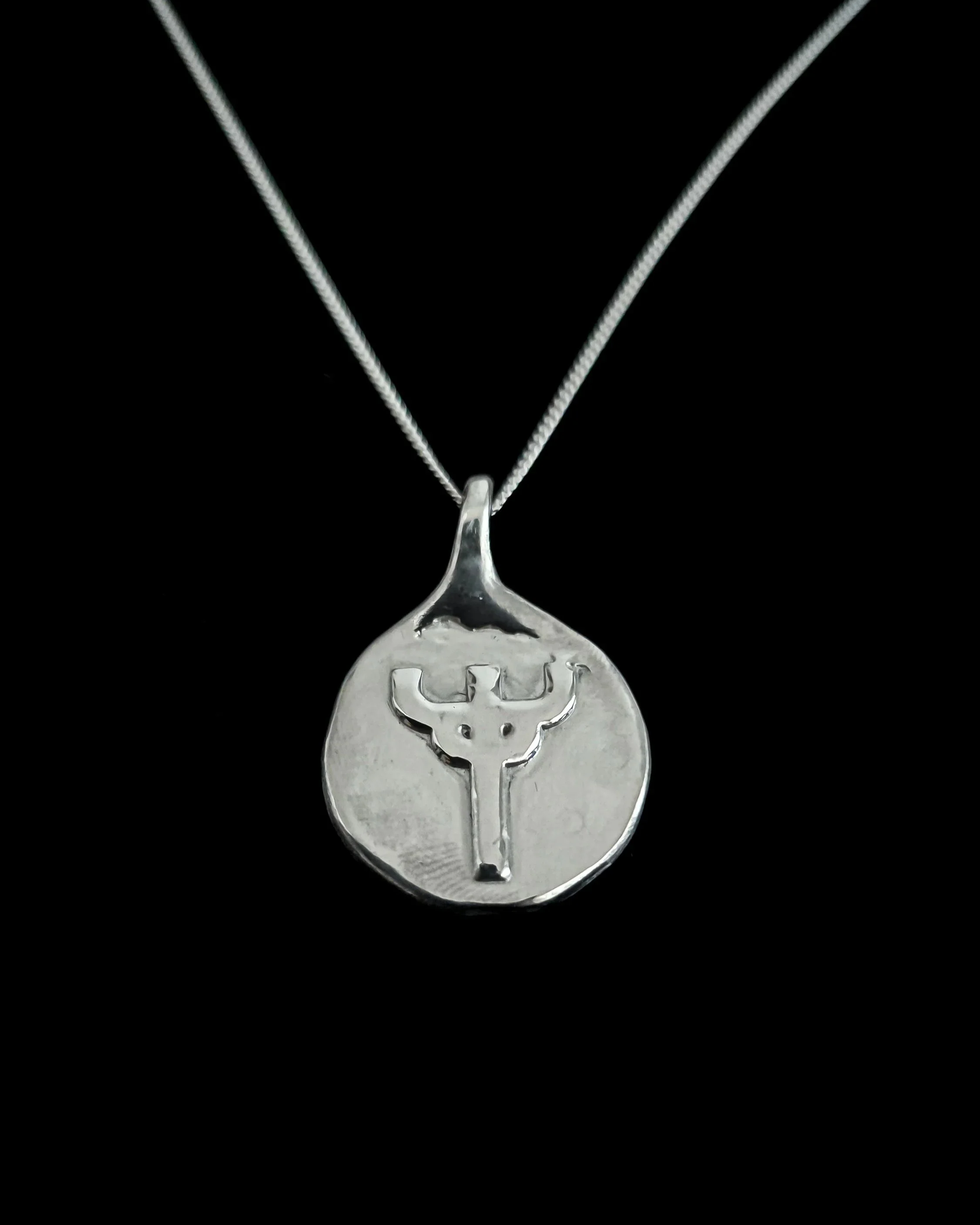 Silver necklace with a pendant featuring a judas priest tuning fork emblem, against a black background.